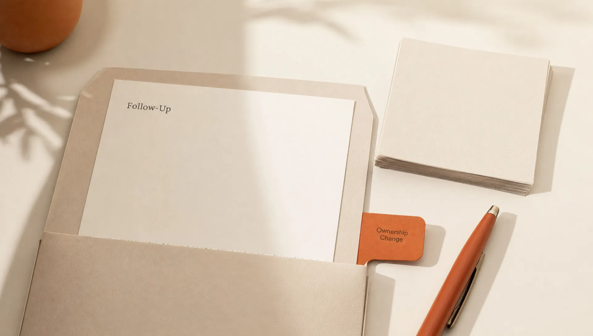 A CRM follow-up packet sits on a table with a blank note card, paper notes, a pen, and a burnt orange tab marking ownership.