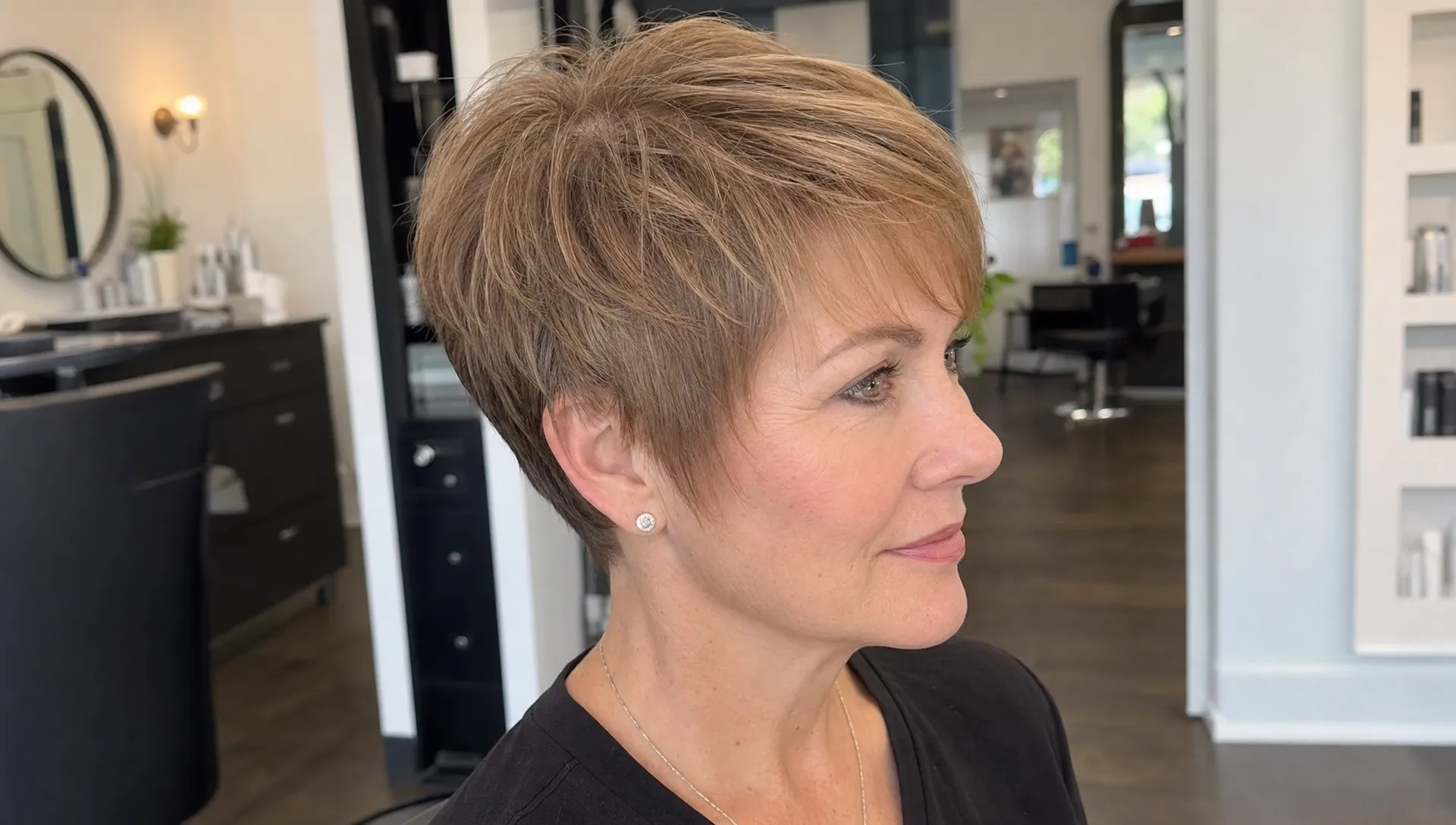 A close-up portrait of a woman in a salon with fine hair shaped into a soft pixie cut, showing crown lift, a neat neckline and side-swept fringe.
