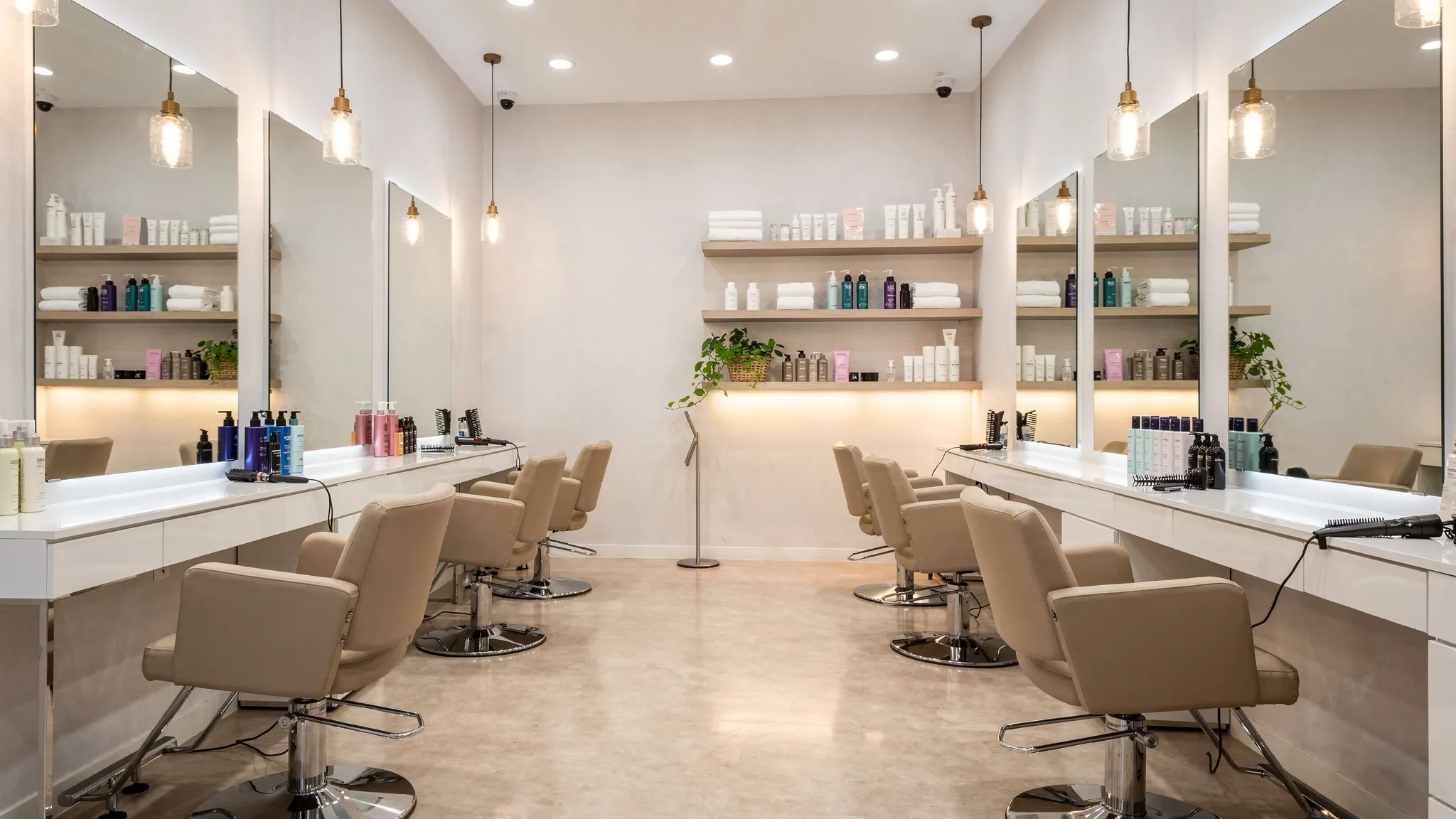 A clean, modern beauty salon interior with styling stations, comfortable chairs, neatly organized professional hair products, and warm welcoming lighting.
