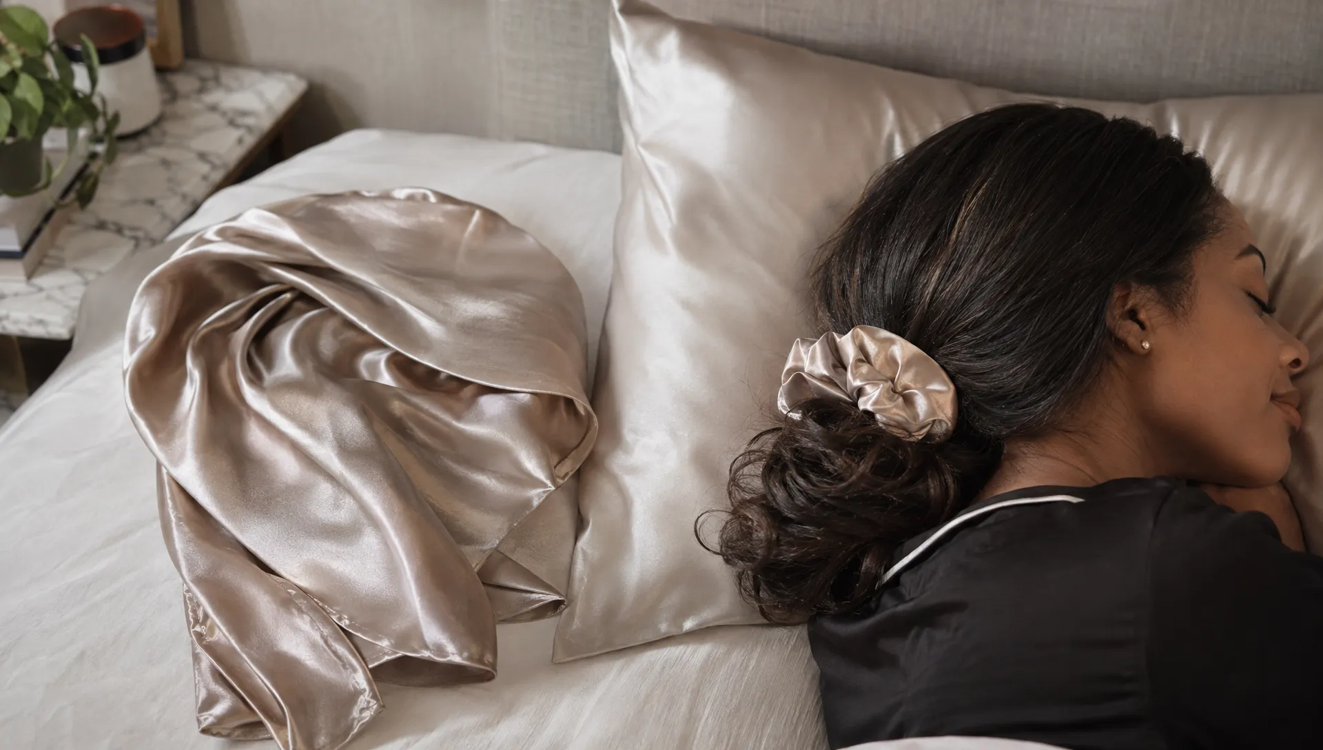 A satin scarf and pillowcase sit beside an adult's loosely secured stretched hair, showing a gentle way to protect a curly hair blowout overnight.