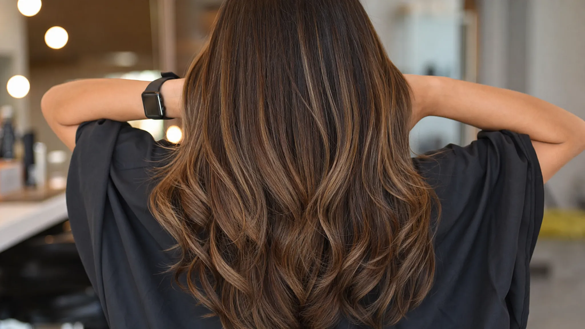 A close-up view of long hair extensions blended into natural hair, showing soft layers, dimensional brunette and caramel tones, and full ends that move seamlessly with the client’s own hair.