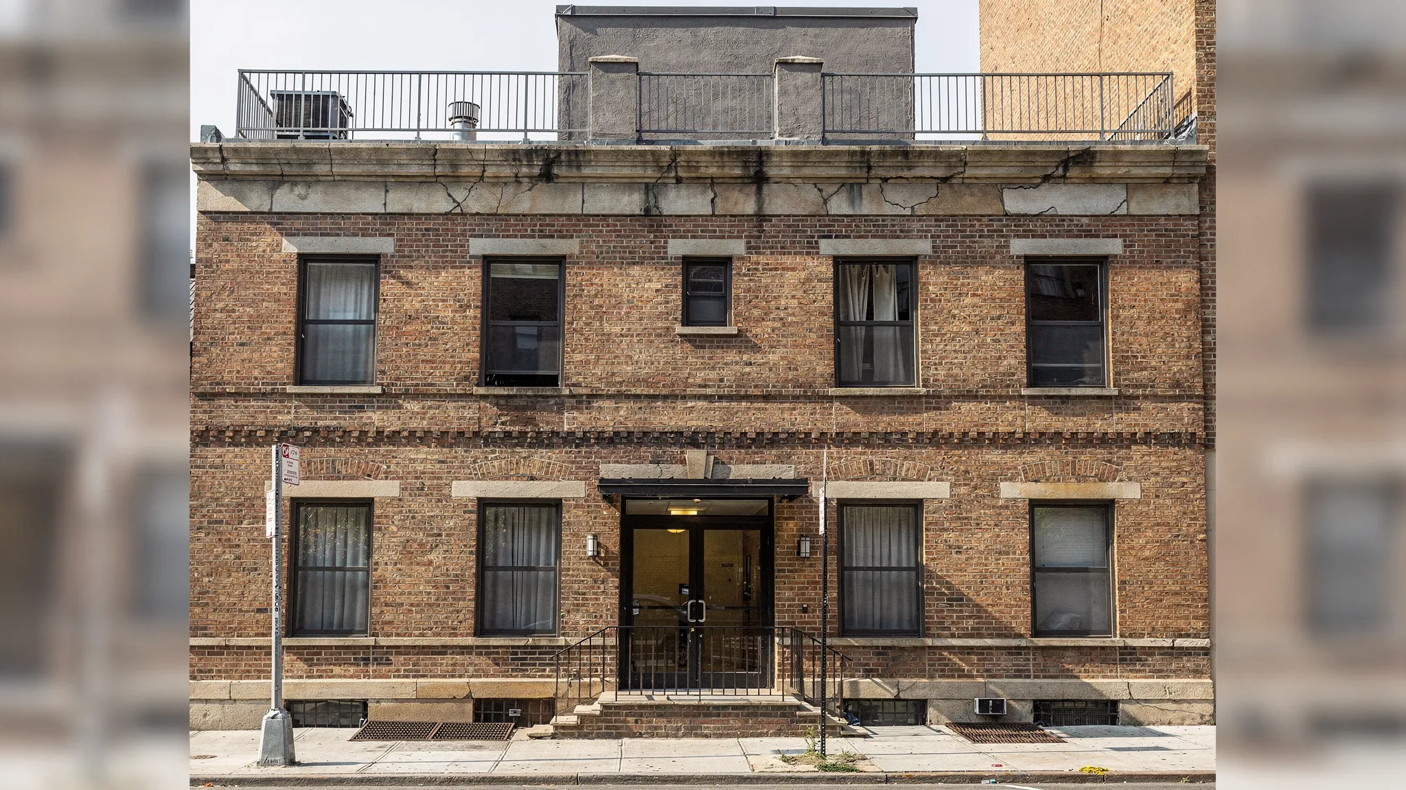 A realistic NYC mid-rise residential building exterior with visible facade details (brick, parapet, lintels), a rooftop bulkhead, and sidewalk-level building entrance; the scene emphasizes maintenance elements boards track like facade condition and roof structures.