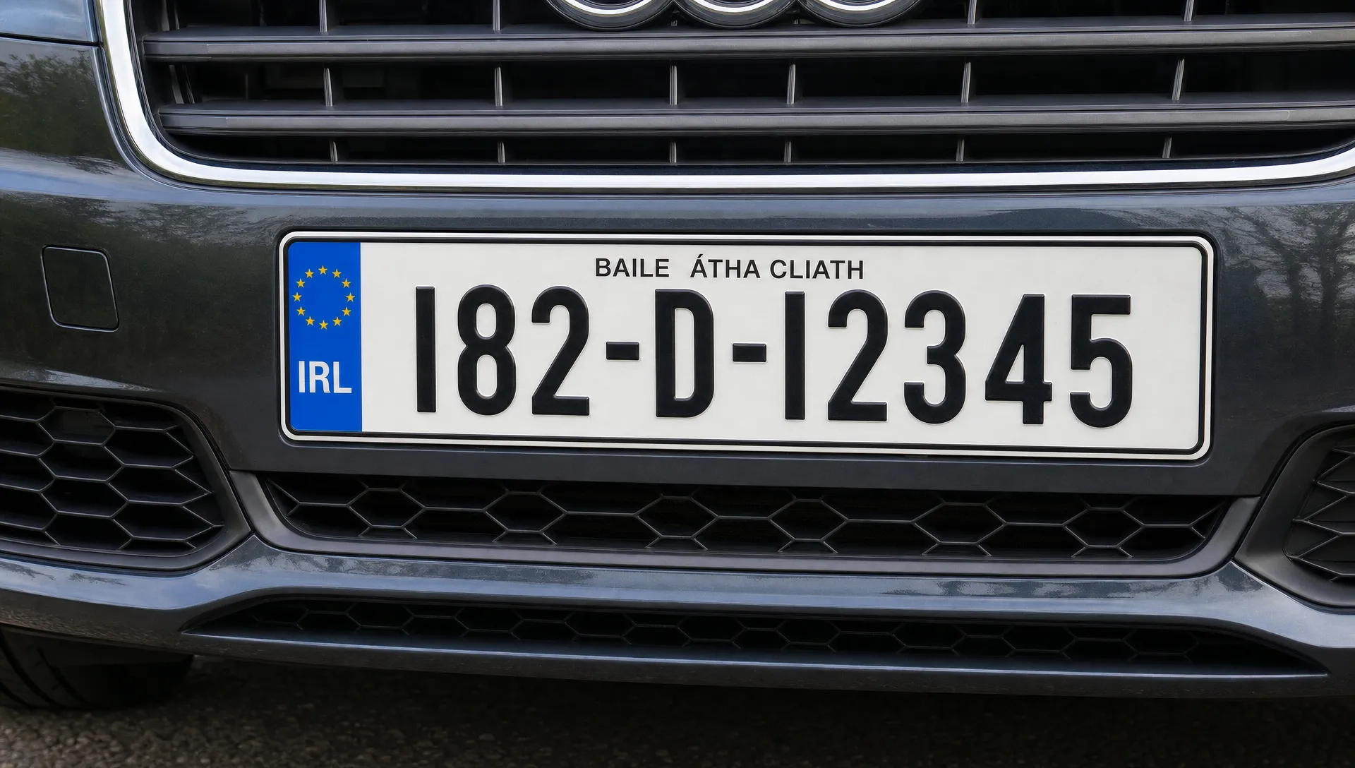A tight close-up of a clean Irish vehicle number plate with raised black characters on a white reflective surface, fitted straight on the bumper of a detailed car outside in daylight.
