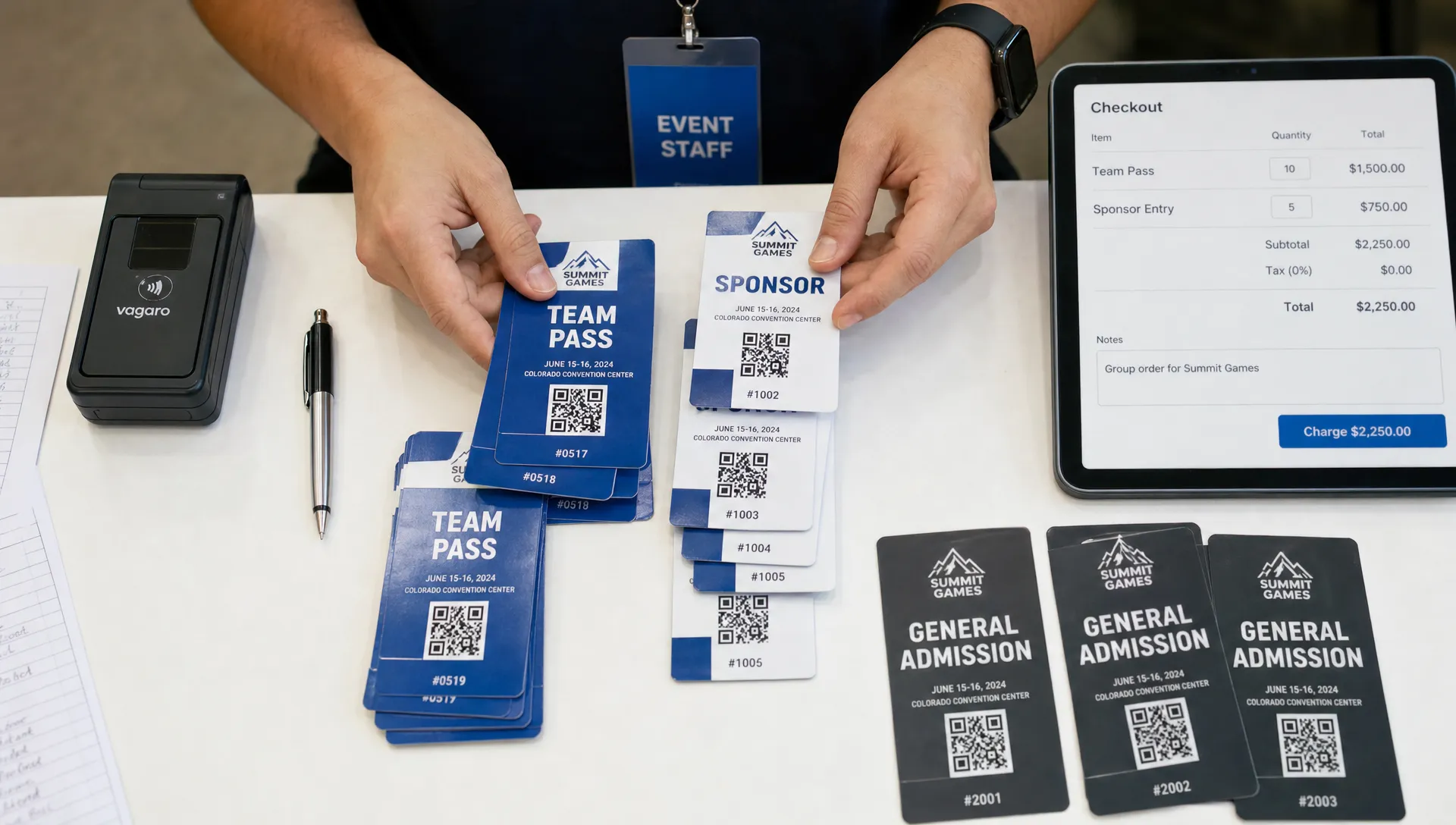 Landscape overhead scene of hands organizing a group ticket order on a registration table, with several admission cards, a pen, a card reader, and a tablet showing checkout fields facing the camera. The hands separate team passes from sponsor entries and match names to quantities in a real working setup.