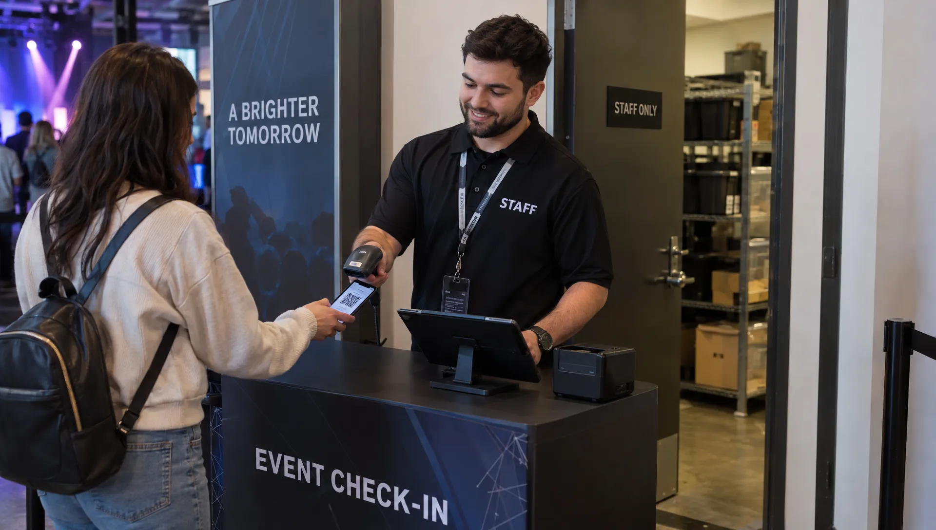 At a venue entrance, a staff member scans an attendee’s ticket while a secured staff-only storage area sits behind the check-in desk.