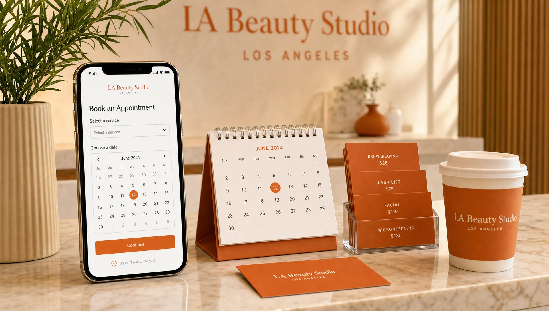 A Los Angeles beauty studio counter with a phone facing the camera showing a simple appointment booking page, a small paper calendar, a cup of coffee, and neatly stacked service price cards.
