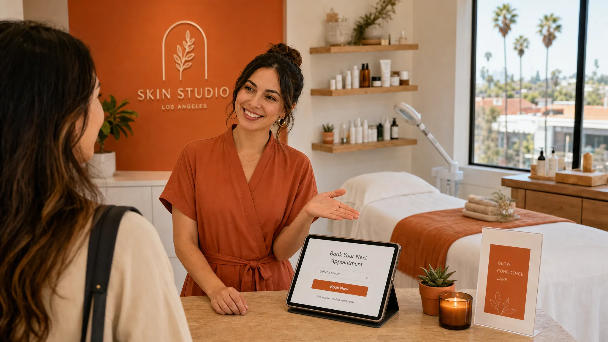 A warm Los Angeles beauty studio interior with an adult esthetician greeting a client near the treatment room entrance, one hand gesturing toward a simple booking tablet on a counter, with a facial bed, folded towels, product shelves, and daylight coming through a window. The scene feels welcoming, local, and easy to trust, with earthy tones and a focus on making the next appointment feel simple.