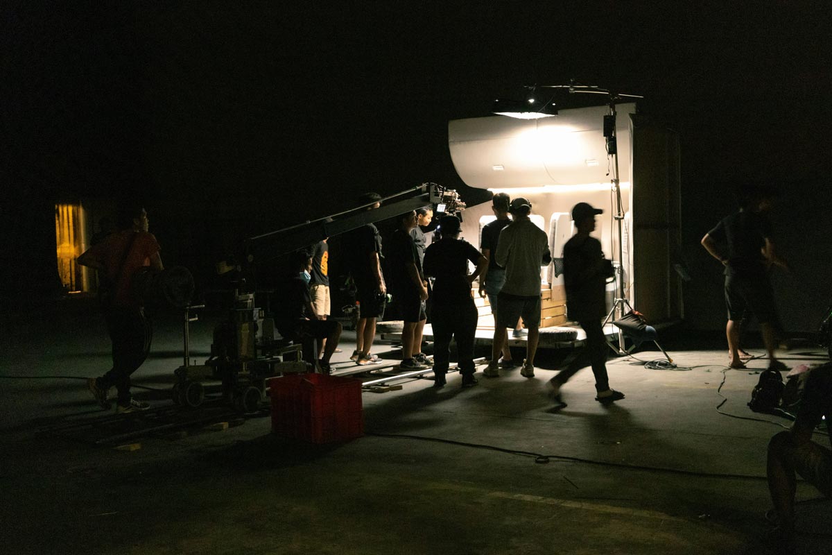 A factory specialist in protective equipment answers interview questions on a Taiwan production floor as a camera crew films beside the marked safety walkway.