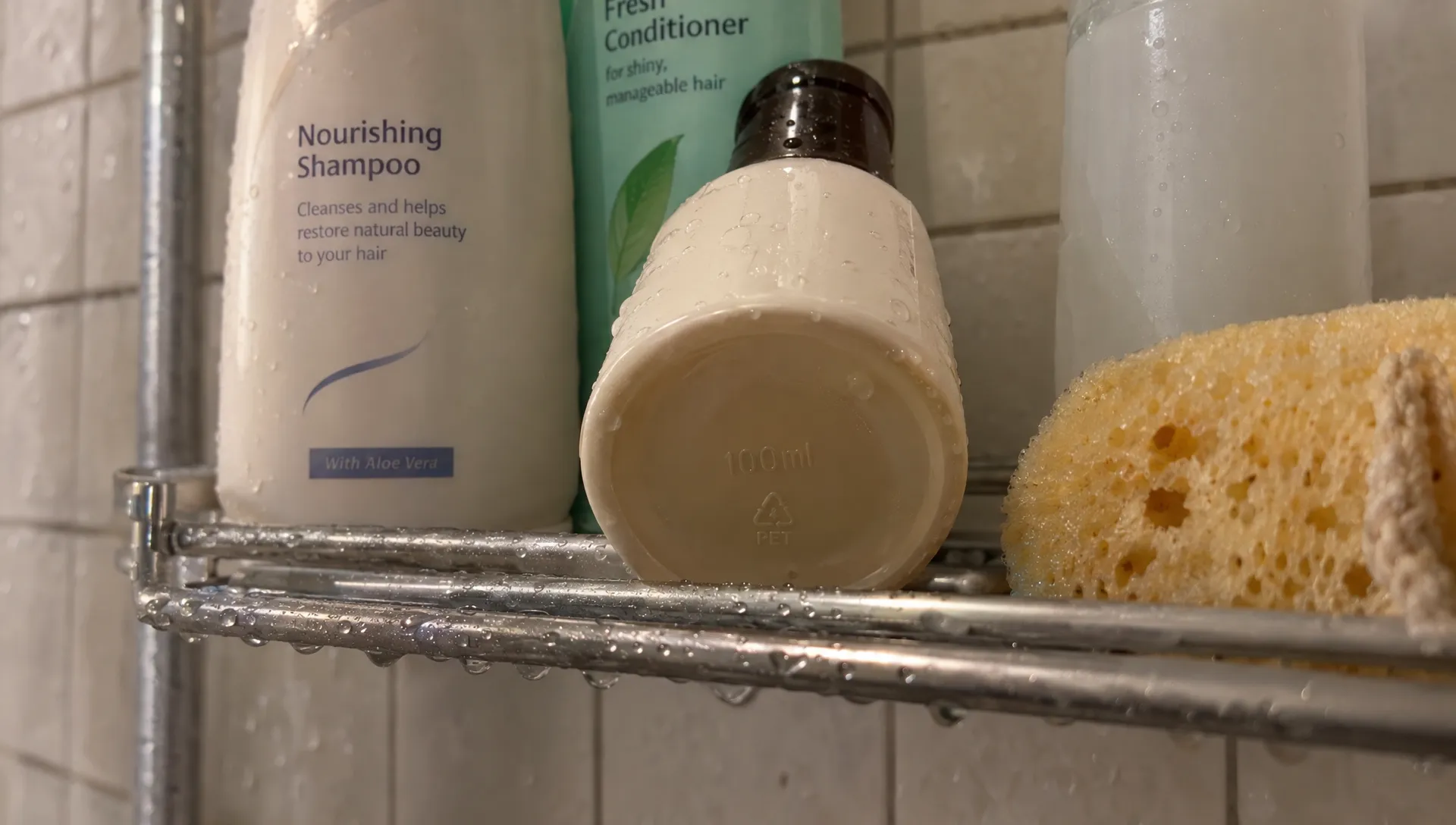 A shampoo bottle marked 100ml sits among bathroom toiletries, showing the container capacity relevant to hand-luggage liquid rules.