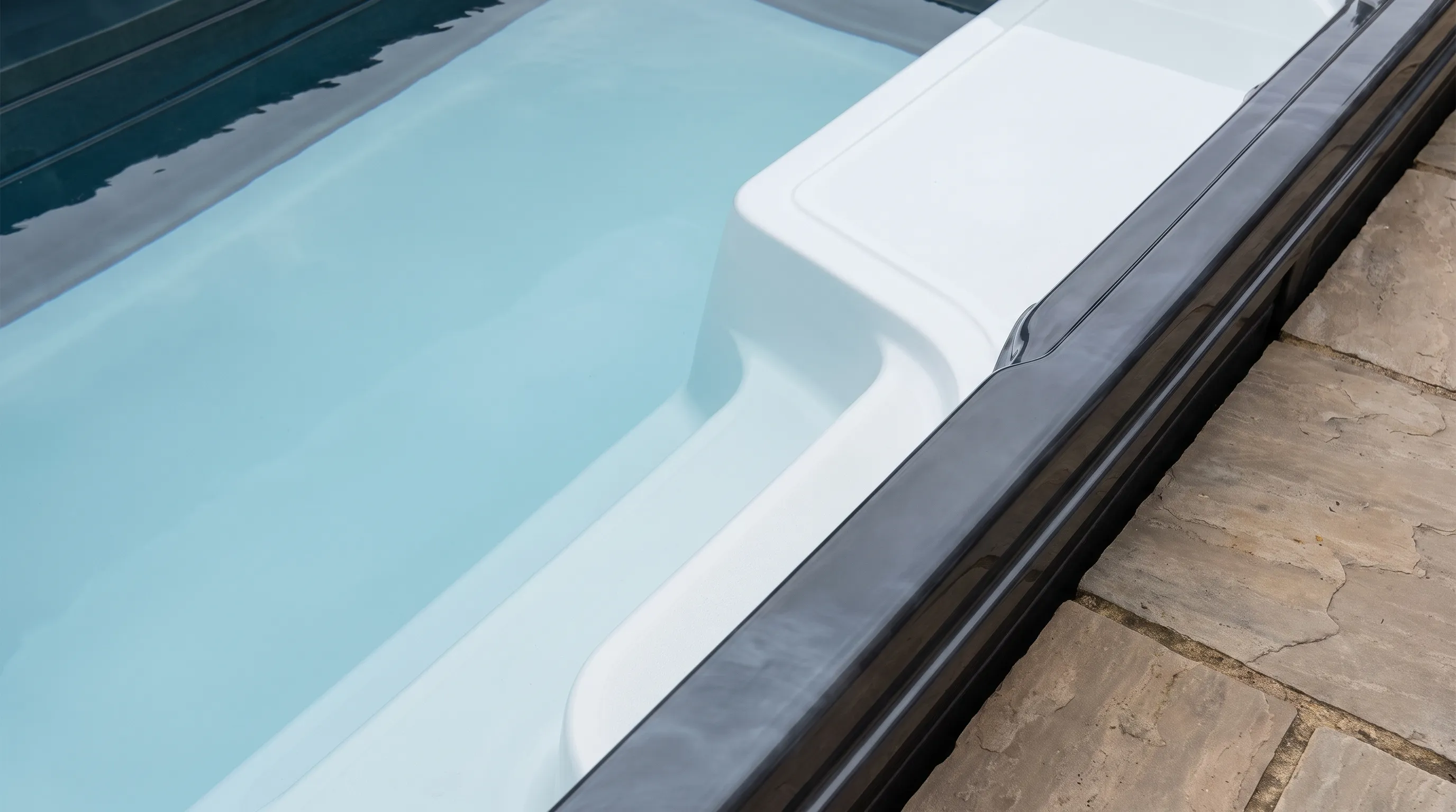 The swim spa interior shows the clear lane beside seating and steps.