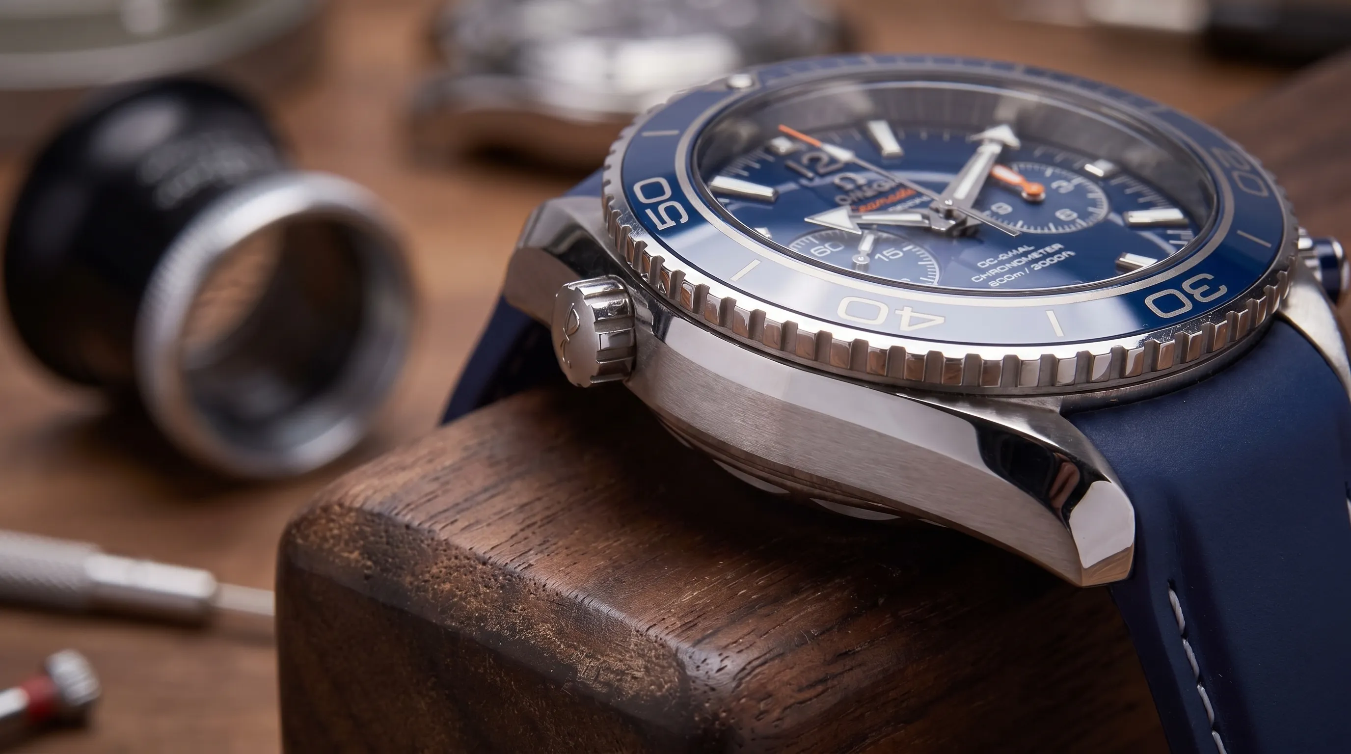 Extreme close-up of an Omega Seamaster Diver 300M case and bezel on a watchmaker’s bench, with a loupe and tools nearby.