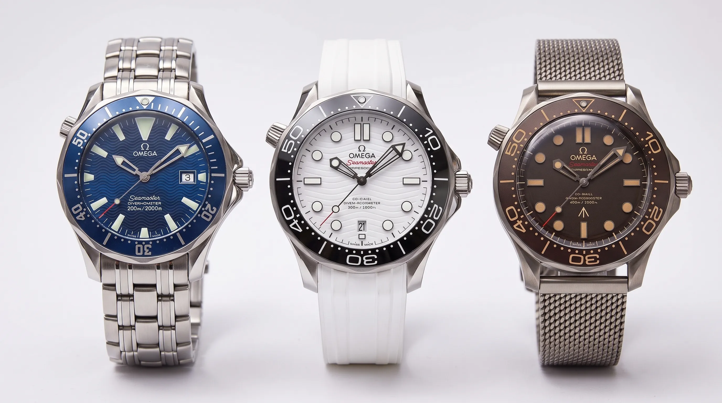 Three Omega Seamaster Diver 300M watches side by side: an early blue wave-dial steel model, a white ceramic wave-dial model, and a brown titanium No Time to Die edition.