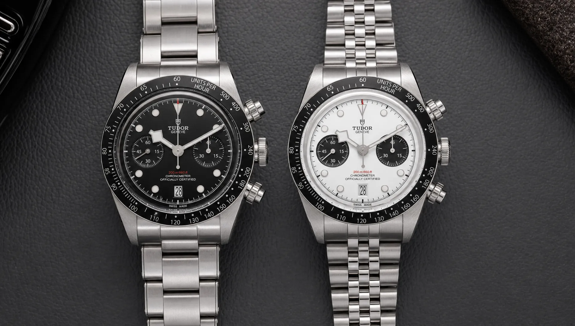 Two Tudor Black Bay Chrono watches sit side by side with contrasting black and white dials, fixed tachymeter bezels, screw-down pushers and different bracelet styles.