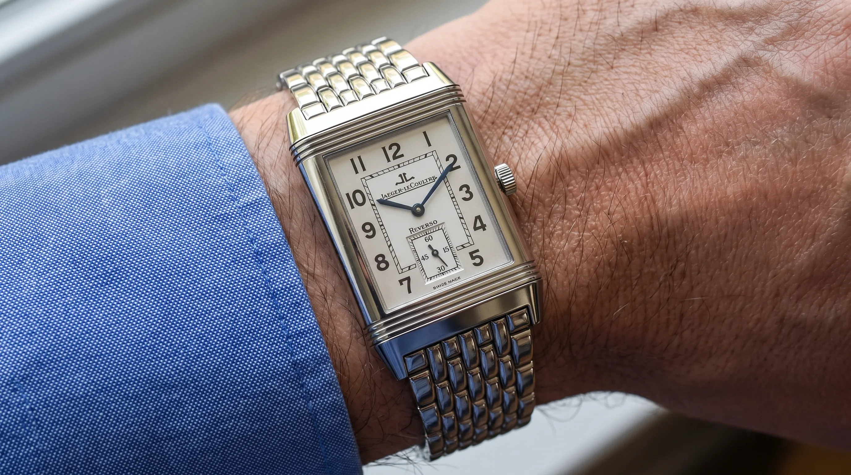 A Cartier Pasha watch on a wrist, seen from above and the side to show the round case, chained crown cap, lug position, and bracelet fit.