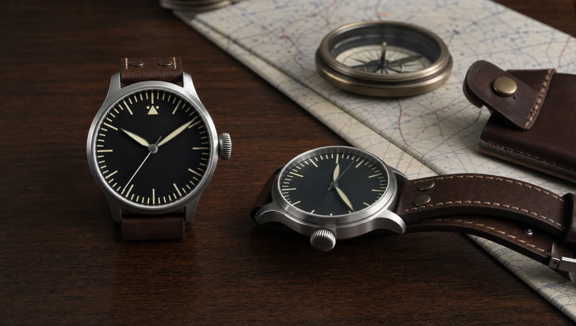 Two aviation-inspired pilot watches sit beside a folded flight map and compass on a desk.