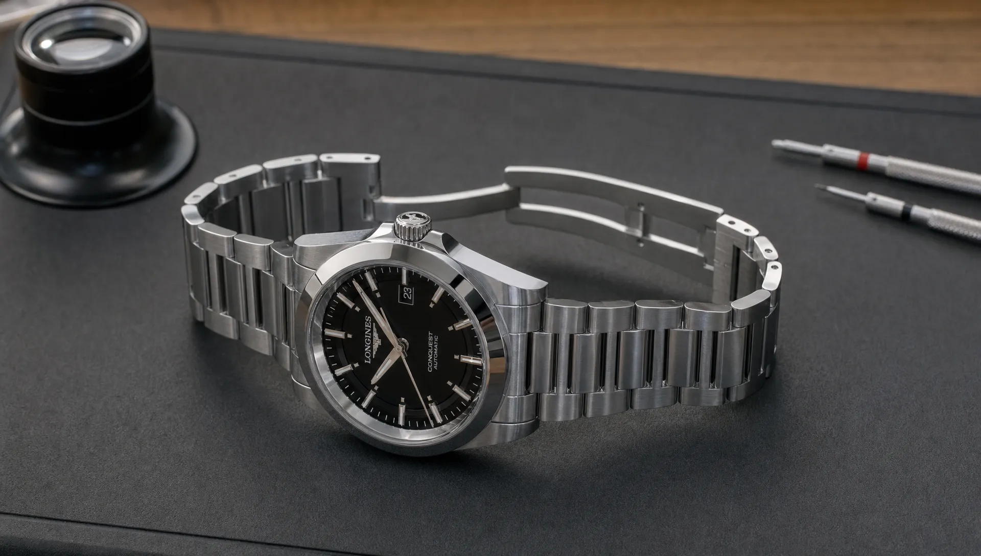 A Longines Conquest rests on an inspection mat with the clasp open and the case sides, crown and bracelet links visible.