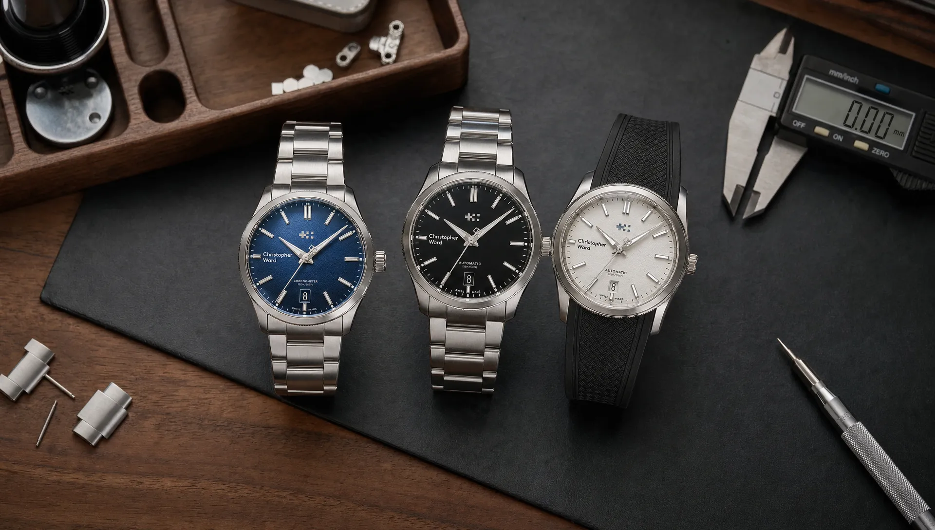 Three Christopher Ward watches are compared on a watchmaker’s bench beside a caliper and spare bracelet links.