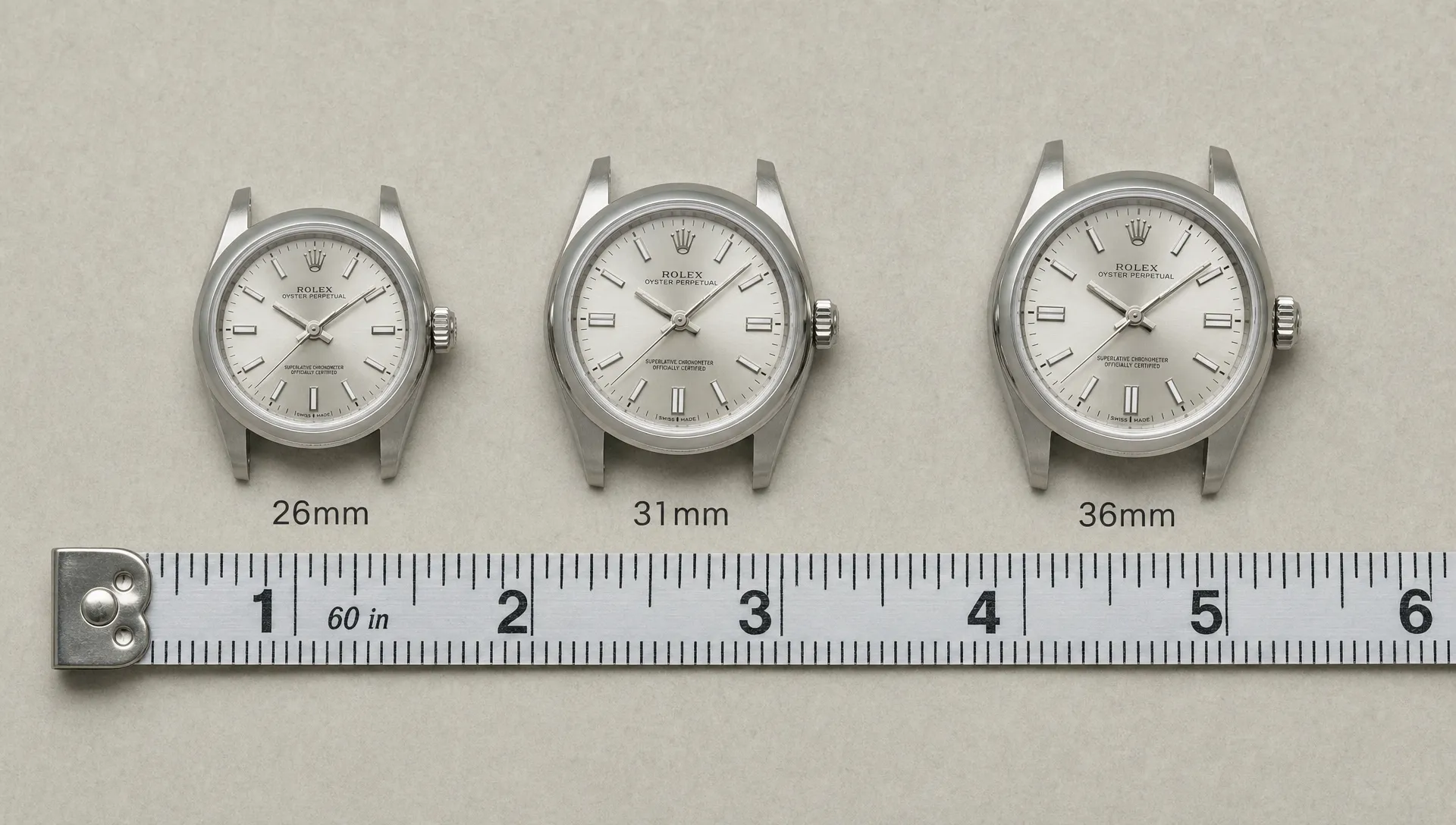 Three Rolex cases in 26mm, 31mm, and 36mm sizes rest beside a measuring tape to compare proportions.