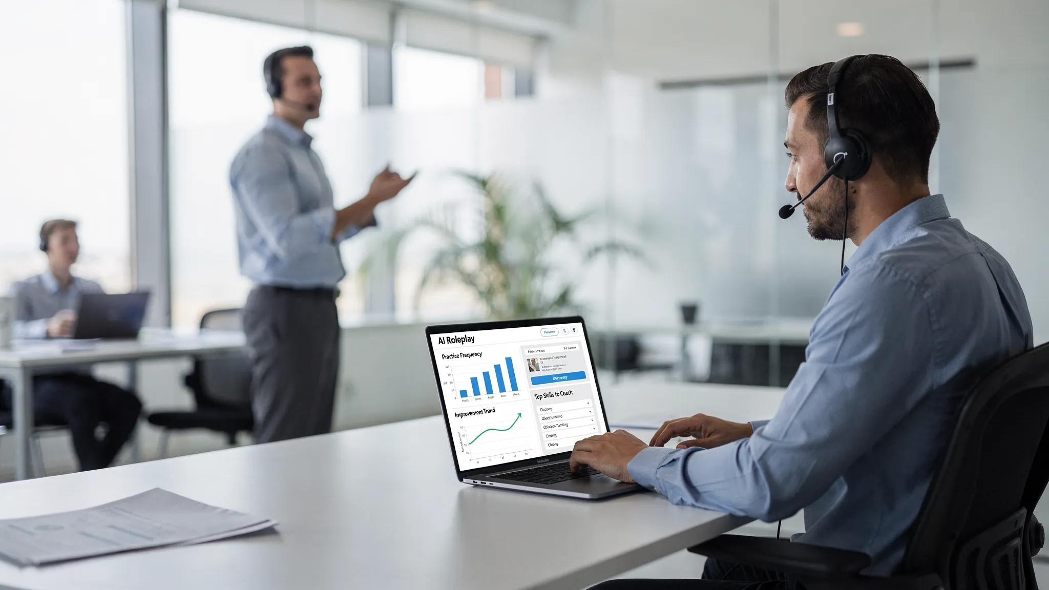 A sales enablement manager reviewing a simple analytics dashboard showing practice frequency, improvement trend lines, and top skills to coach, with a rep practicing an AI roleplay scenario nearby in an office setting.