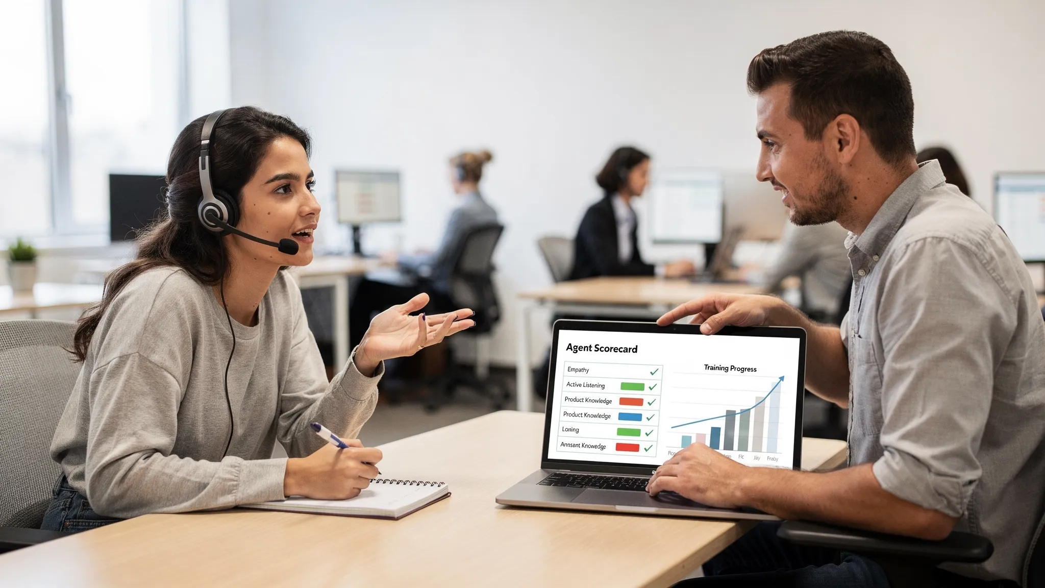 A customer support training scene where one agent practices a roleplay conversation while a team lead reviews a simple scorecard and progress chart on a laptop screen facing the right direction. The setting looks like a modern office training area.
