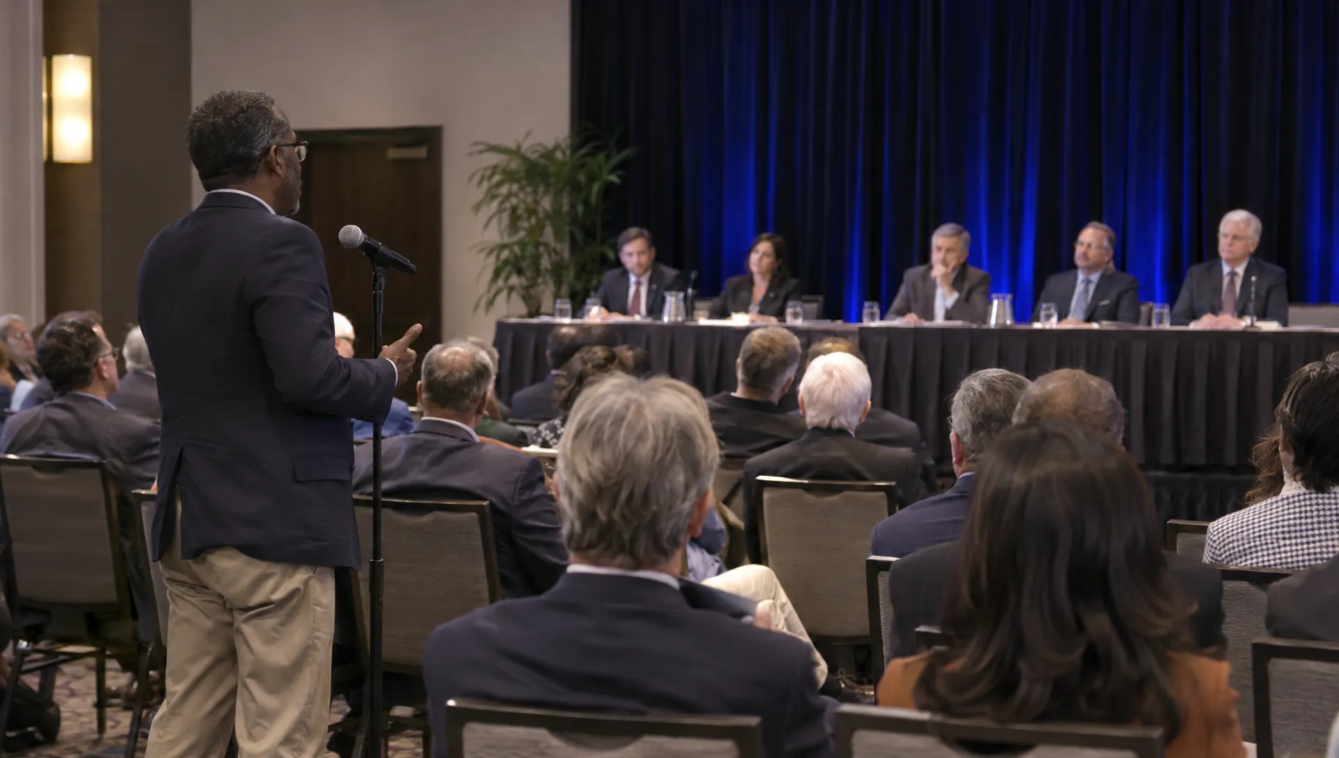 A shareholder questions company directors at an annual meeting, raising the accountability concerns tied to concentrated ownership.