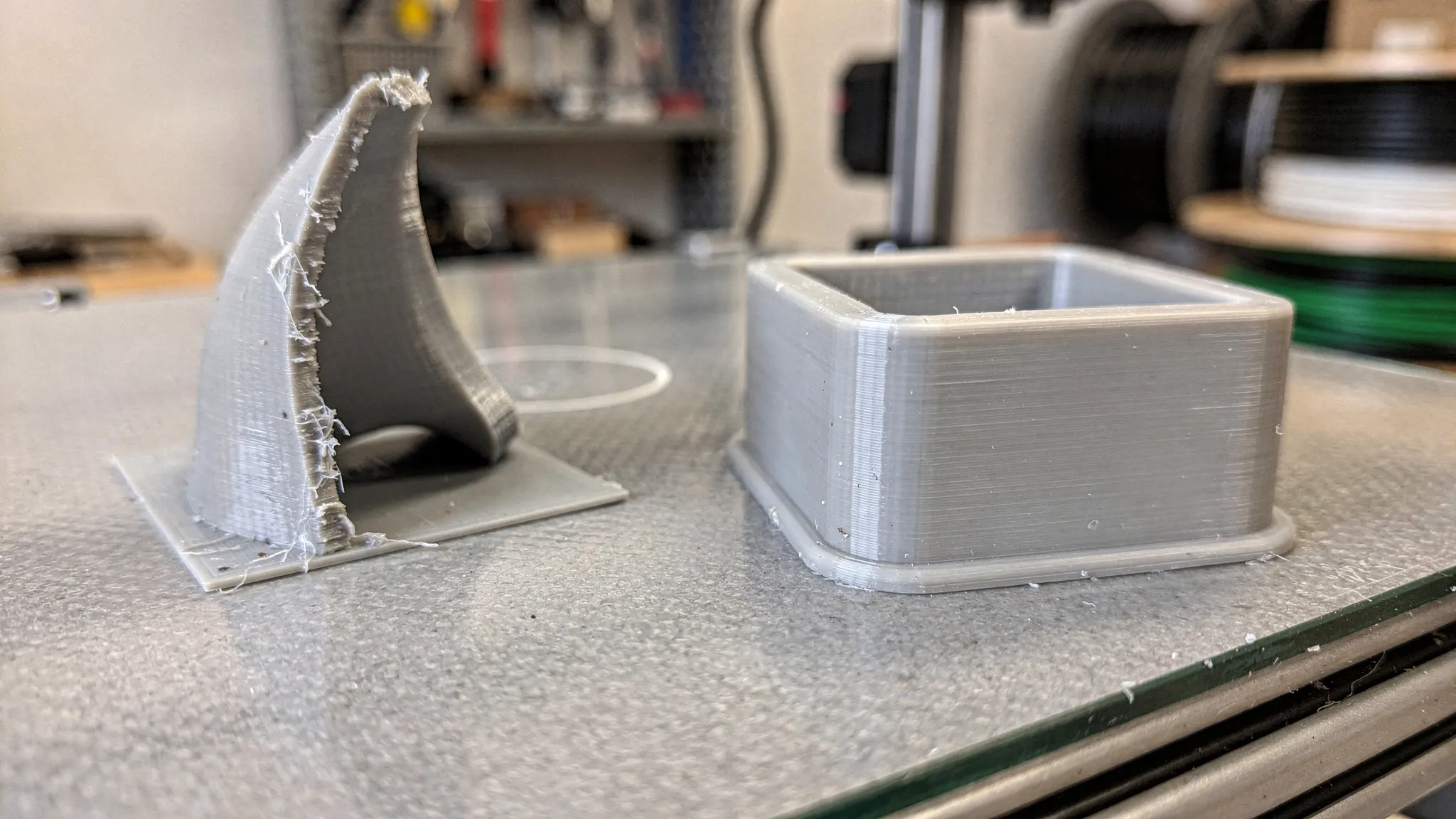 A partially printed 3D model on a print bed with one corner lifting upward, shown next to a clean redesigned version with rounded corners and a stable base.