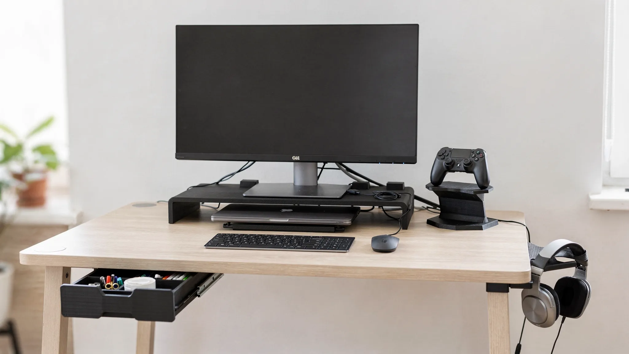 A modern desk setup with 3D printed accessories: a monitor riser, a headphone hanger, cable clips, a controller stand, and a small under-desk drawer, arranged neatly with a laptop and keyboard.