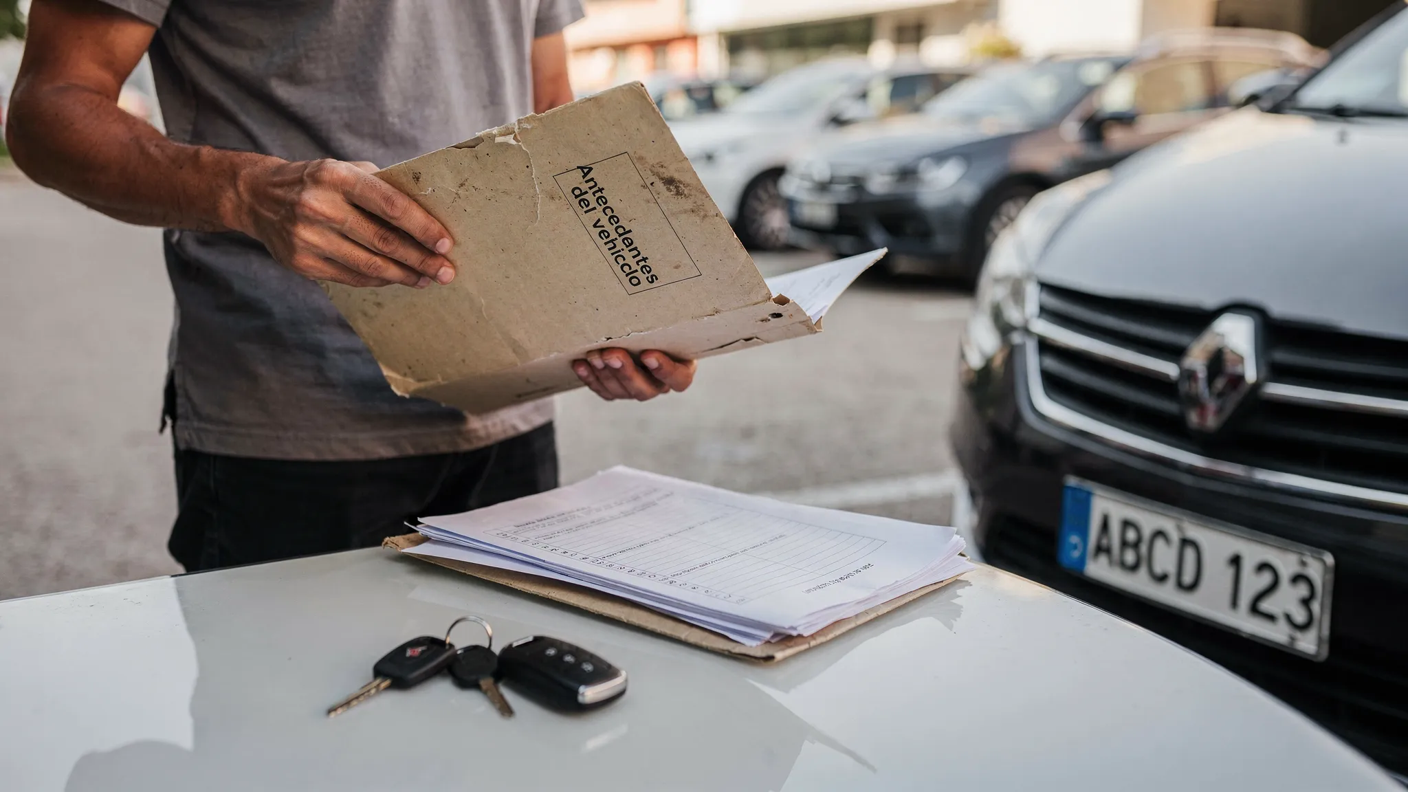 Persona revisando documentos de un auto usado junto a un vehículo estacionado, con una carpeta de antecedentes, llaves del auto y una patente visible en primer plano.
