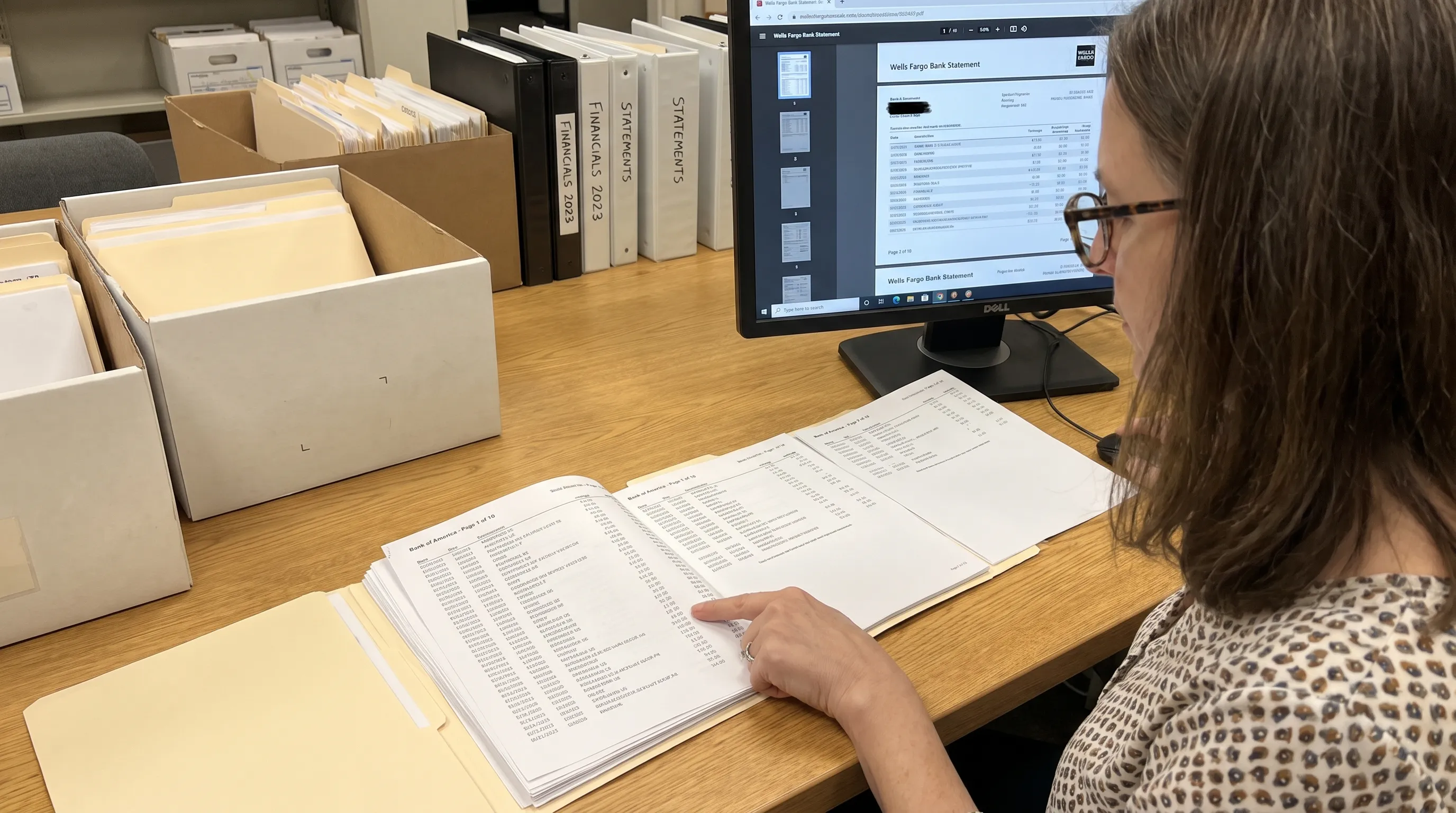 A person compares a scanned bank statement PDF on a monitor with the complete paper pages and their visible numbers.