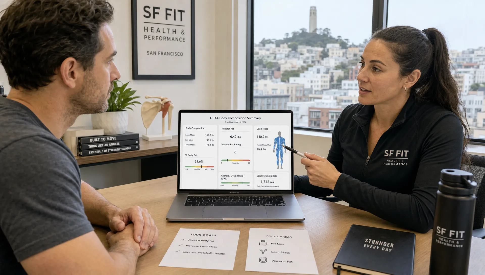 Landscape medium-wide scene in a San Francisco fitness clinic office where an adult client sits with a clinician at a desk reviewing a DEXA body composition summary, with both people visible and the report, pen, and laptop arranged between them. The screen faces the camera and shows a body composition dashboard without anything behind it, while a water bottle and notebook sit off to one side. Keep the conversation focused on fat loss, lean mass, and visceral fat in a real consult setting.