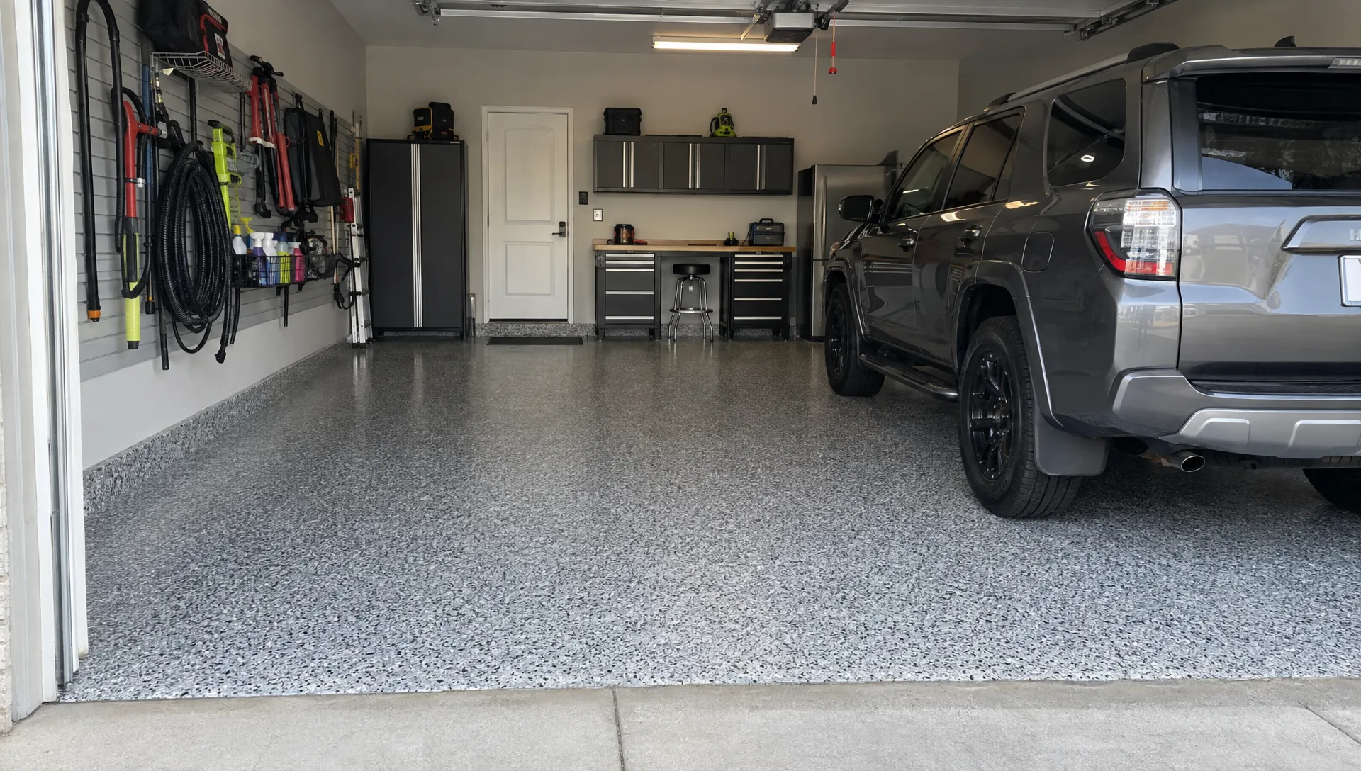 A completed garage floor coating with decorative flakes, clean edges at the doorway, a parked vehicle, and organized wall storage.