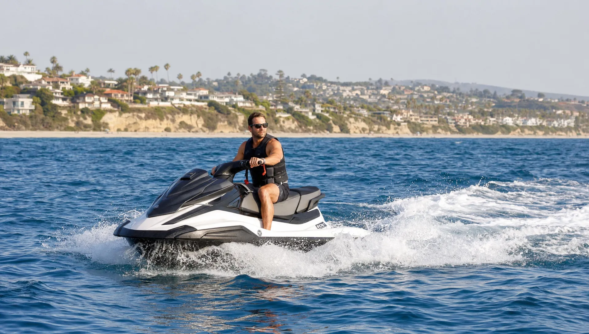 A personal watercraft riding through moderate ocean chop near a Southern California coastline, with the rider wearing a life jacket and keeping clear open water around the craft.