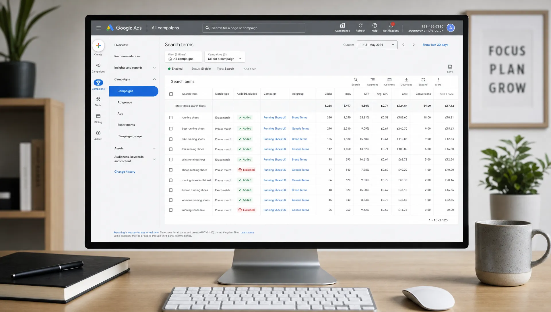 A desktop screen facing the camera showing a Google Ads workspace with organised campaign labels, performance columns and filtered search term data, beside a tidy agency desk with a notebook and pen, no people present.