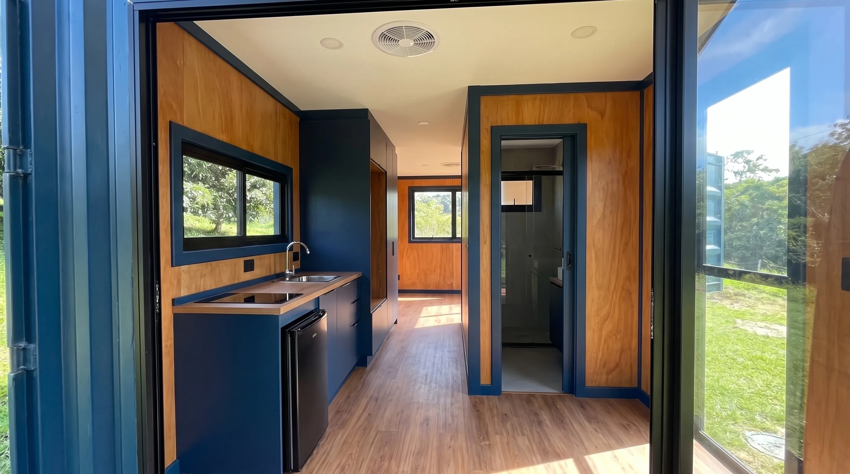 Finished container home interior with a kitchenette, bathroom doorway, and visible window openings.