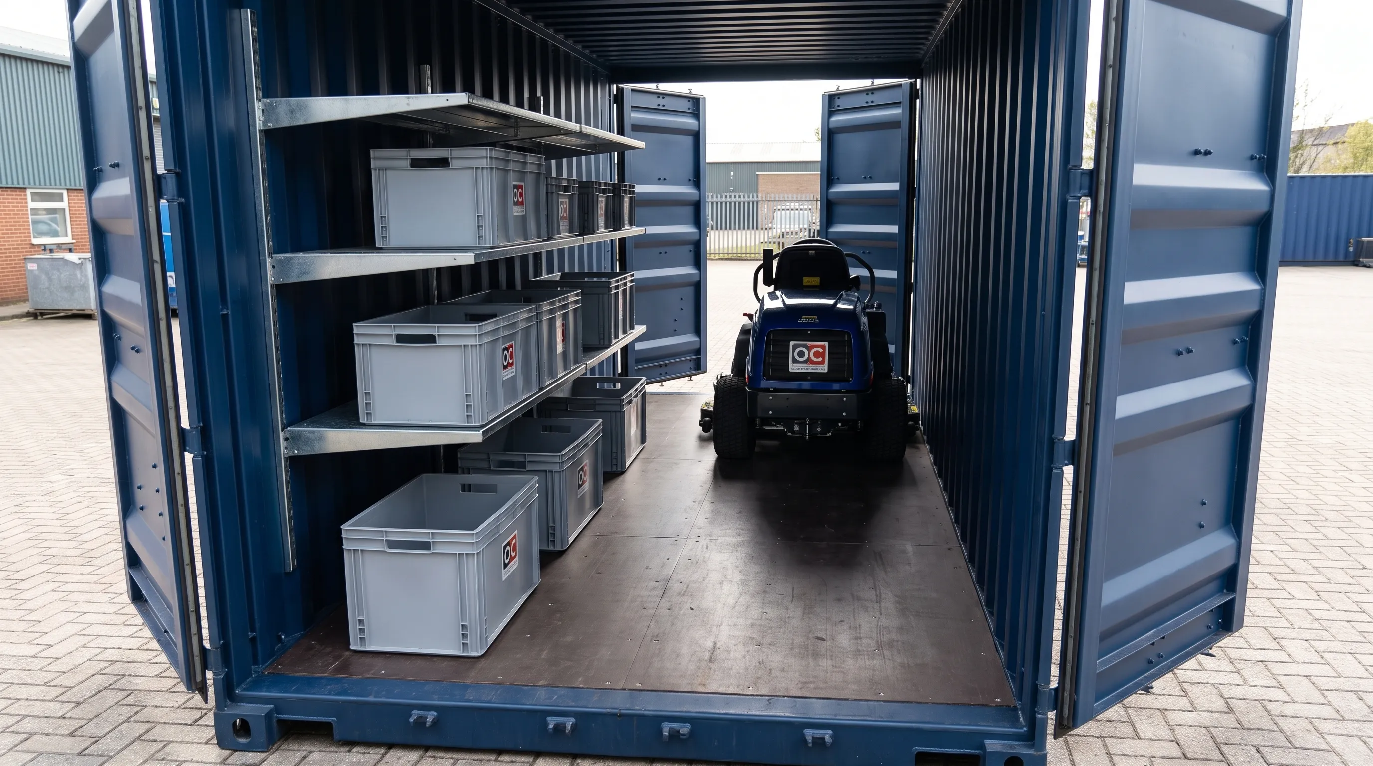 A 20ft cargo container interior has secured shelving, plain storage bins, a compact mower by the open end doors and a clear central aisle for access.