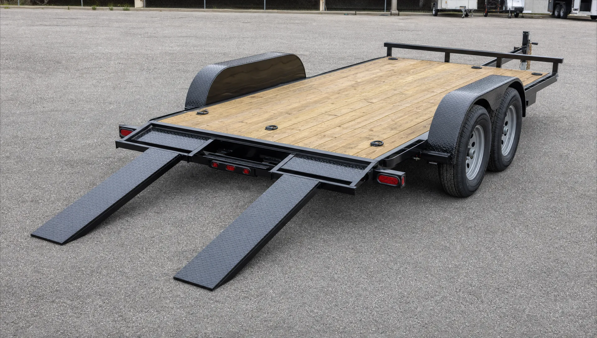 An open car trailer on level pavement shows its loading ramps, wheel fenders, tie-down points and coupler during an inspection.
