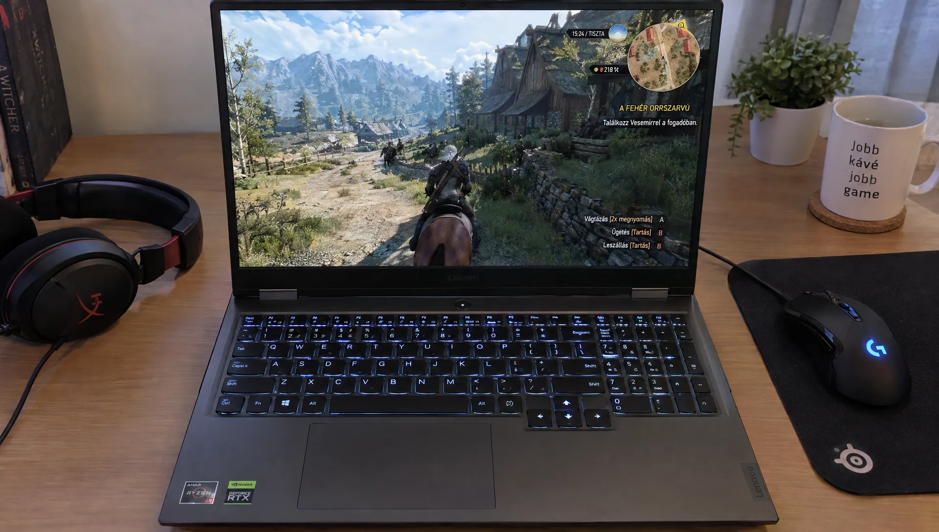 Nyitott gamer laptopon fut egy részletgazdag játékjelenet, mellette egér és fejhallgató látható az asztalon.