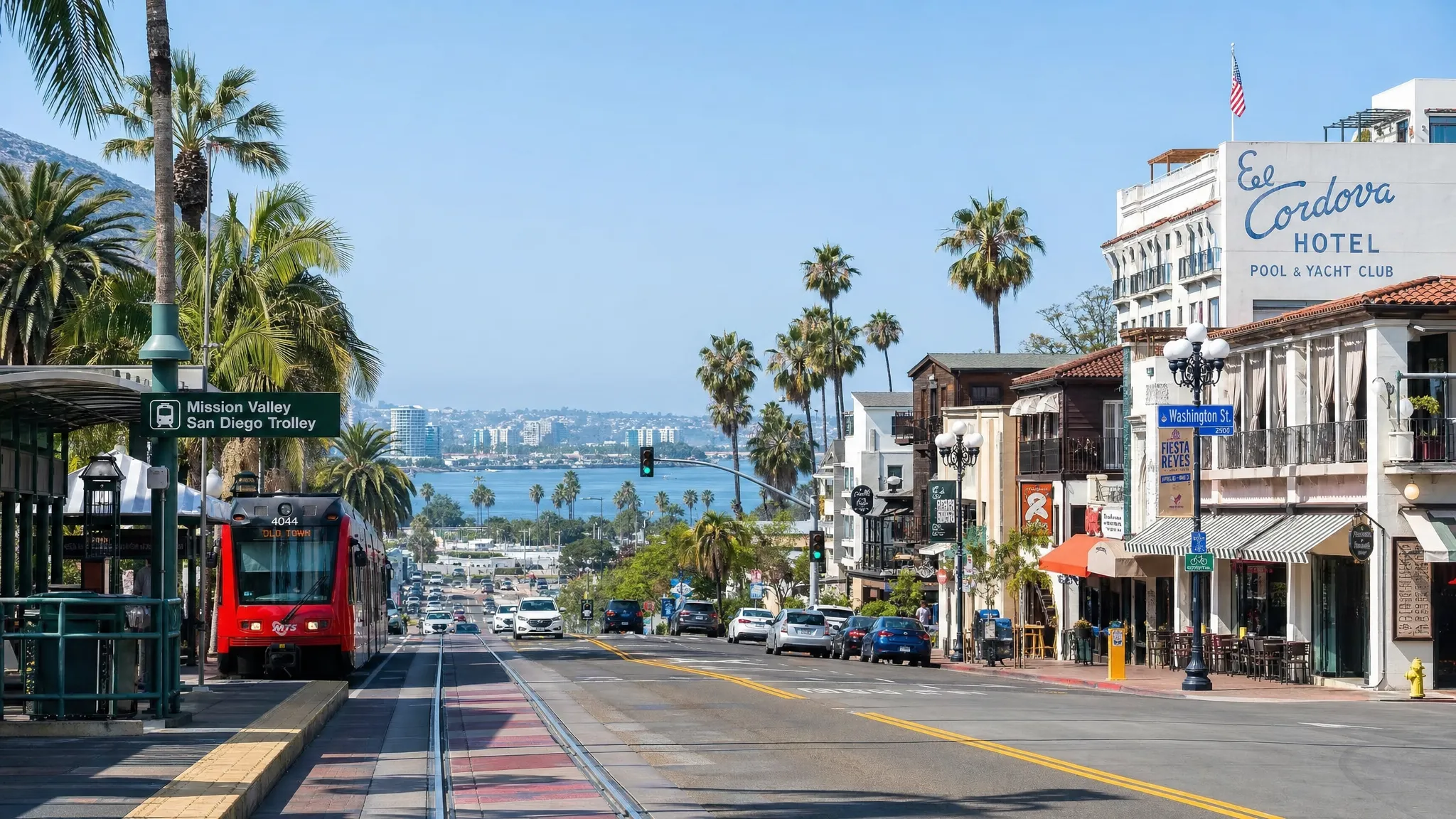 A San Diego street-level scene with palm trees, a trolley stop, low-rise hotels, and the bay in the distance, showing the connection between Downtown, Mission Valley, and the coast across the city.