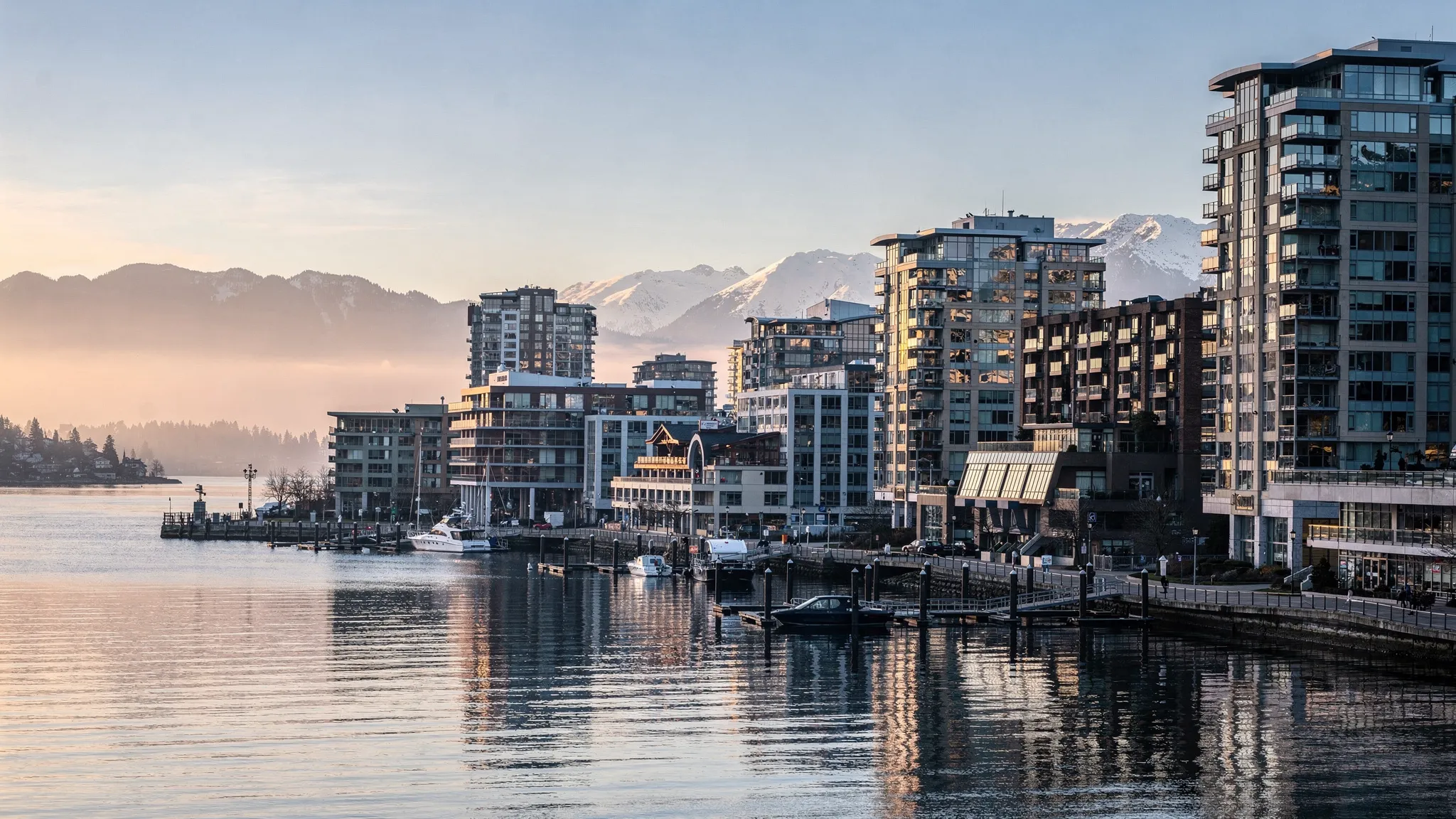 A vivid waterfront cityscape with Vancouver’s harbor in the foreground, mountains in the distance, and modern hotel buildings along the shoreline, capturing a crisp morning with soft light and calm water.