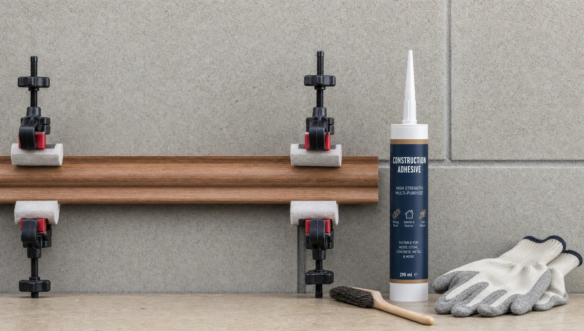 A wooden trim piece is held against a clean masonry surface with padded clamps beside an adhesive cartridge, cleaning brush and protective gloves.