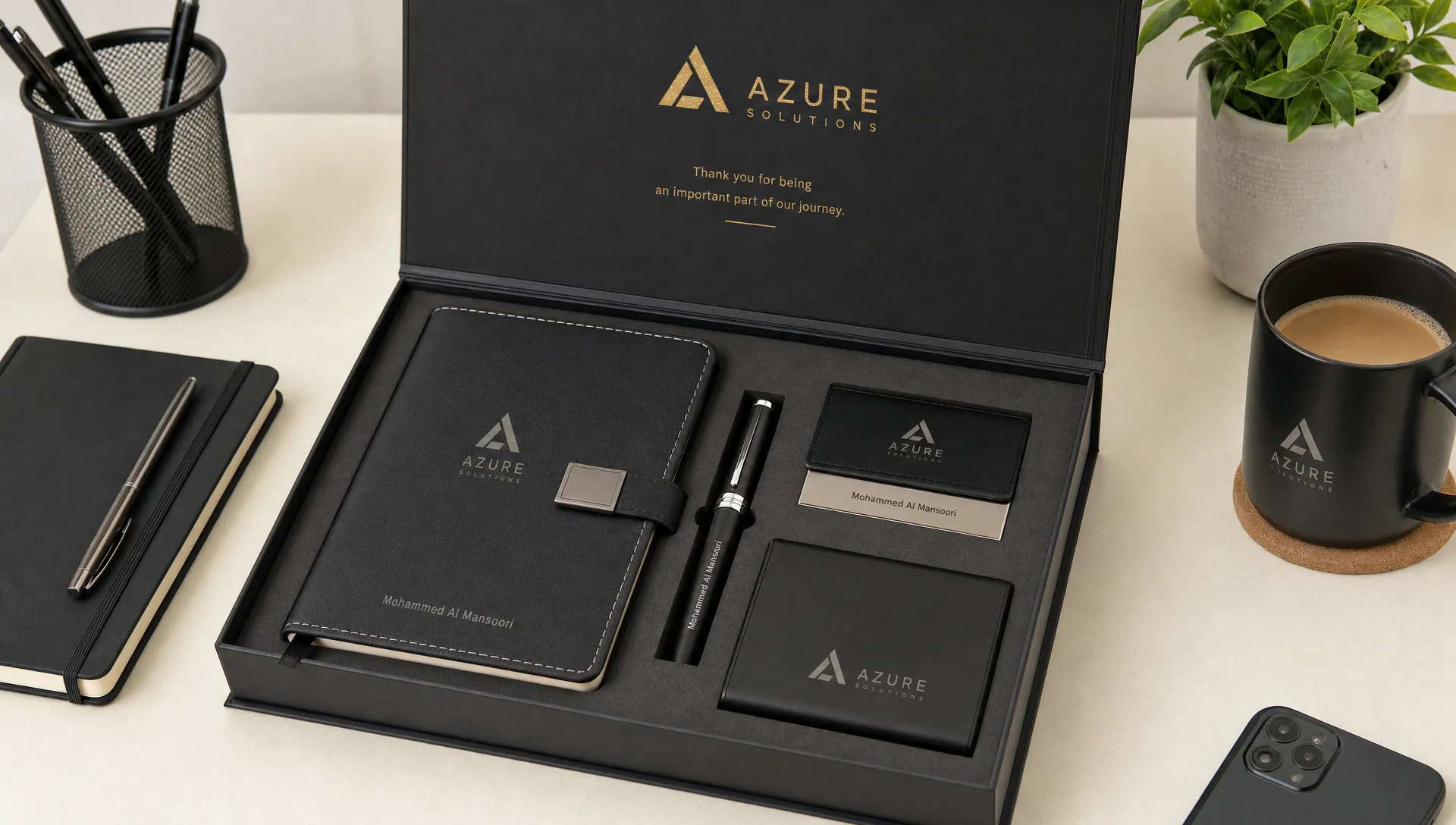 A branded gift box with personalized ink pens, notebooks and stationery arranged on a clean office desk.