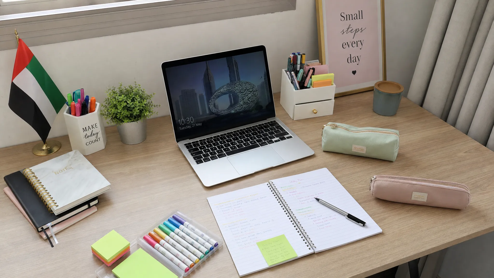 A neatly organised UAE home study desk with notebooks, pens, pencil cases, sticky notes, and a small desk organiser arranged beside a laptop, viewed from a slightly higher angle with no people present.