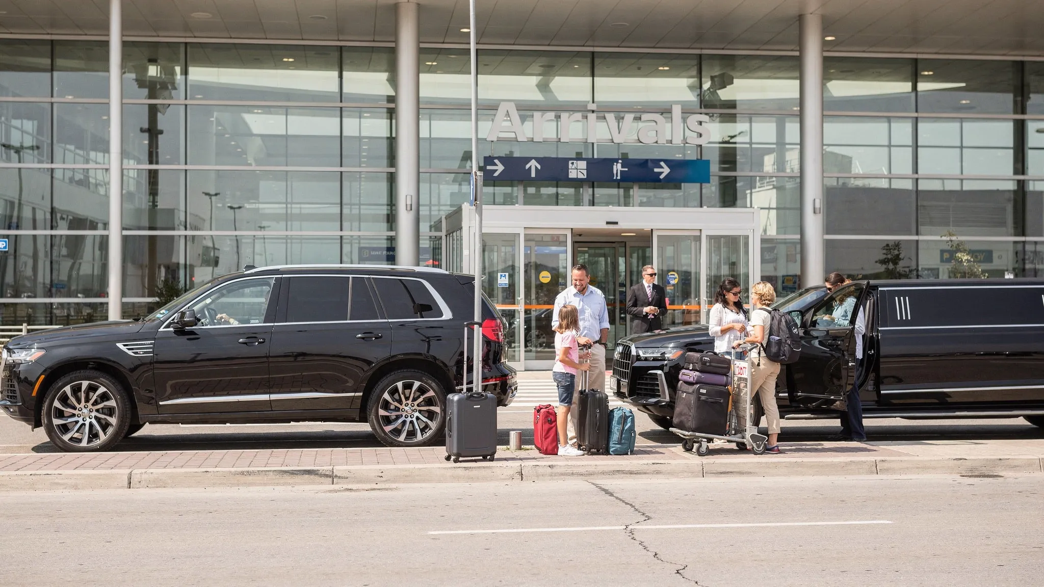 A luxury black SUV and stretch limousine waiting outside an airport arrival area with luggage carts nearby, showing a family and small travel group preparing for a comfortable airport transfer.