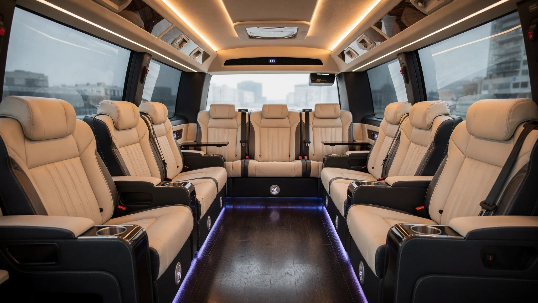A luxury bus limo interior with premium leather seating arranged in a lounge layout, soft ambient lighting along the ceiling, tinted windows, and a clean aisle designed for comfortable group travel.