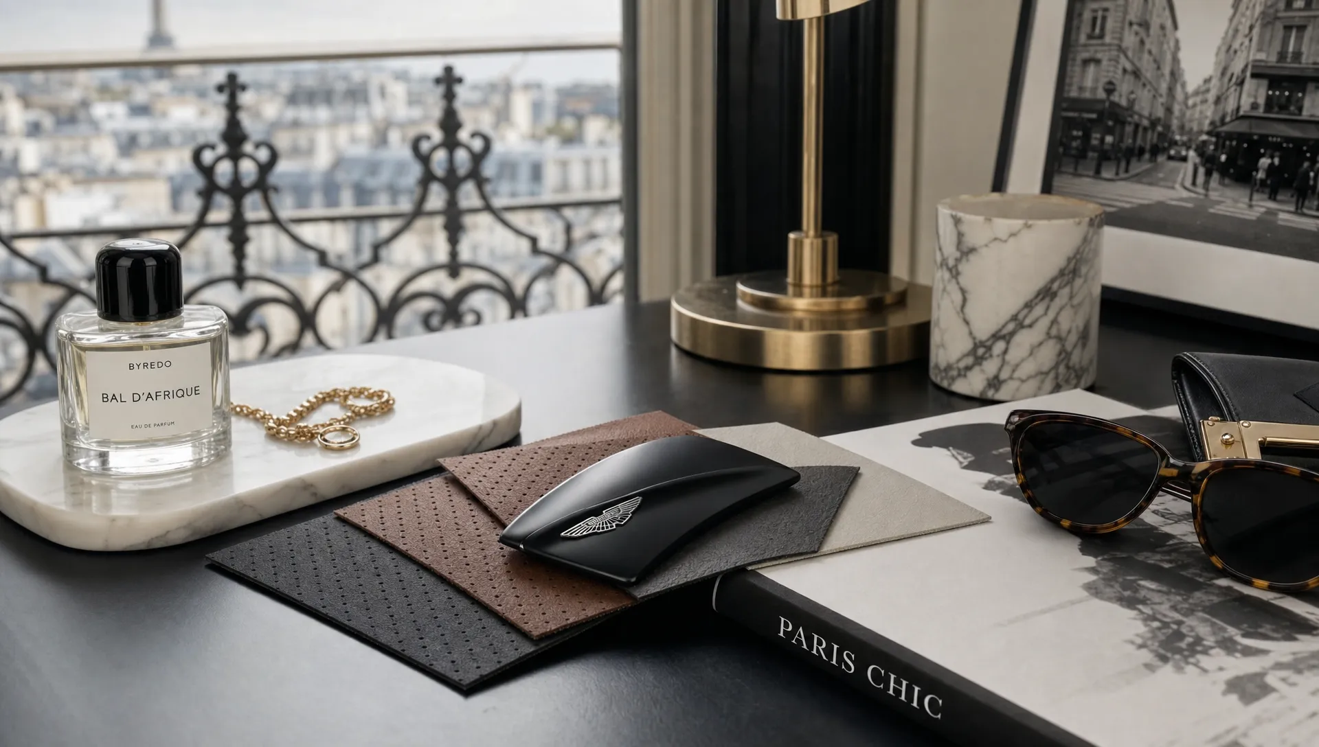 A refined indoor still life with a perfume bottle, a fine jewelry detail, automotive material samples, and fashion accessories arranged on separate surfaces in a Paris studio.