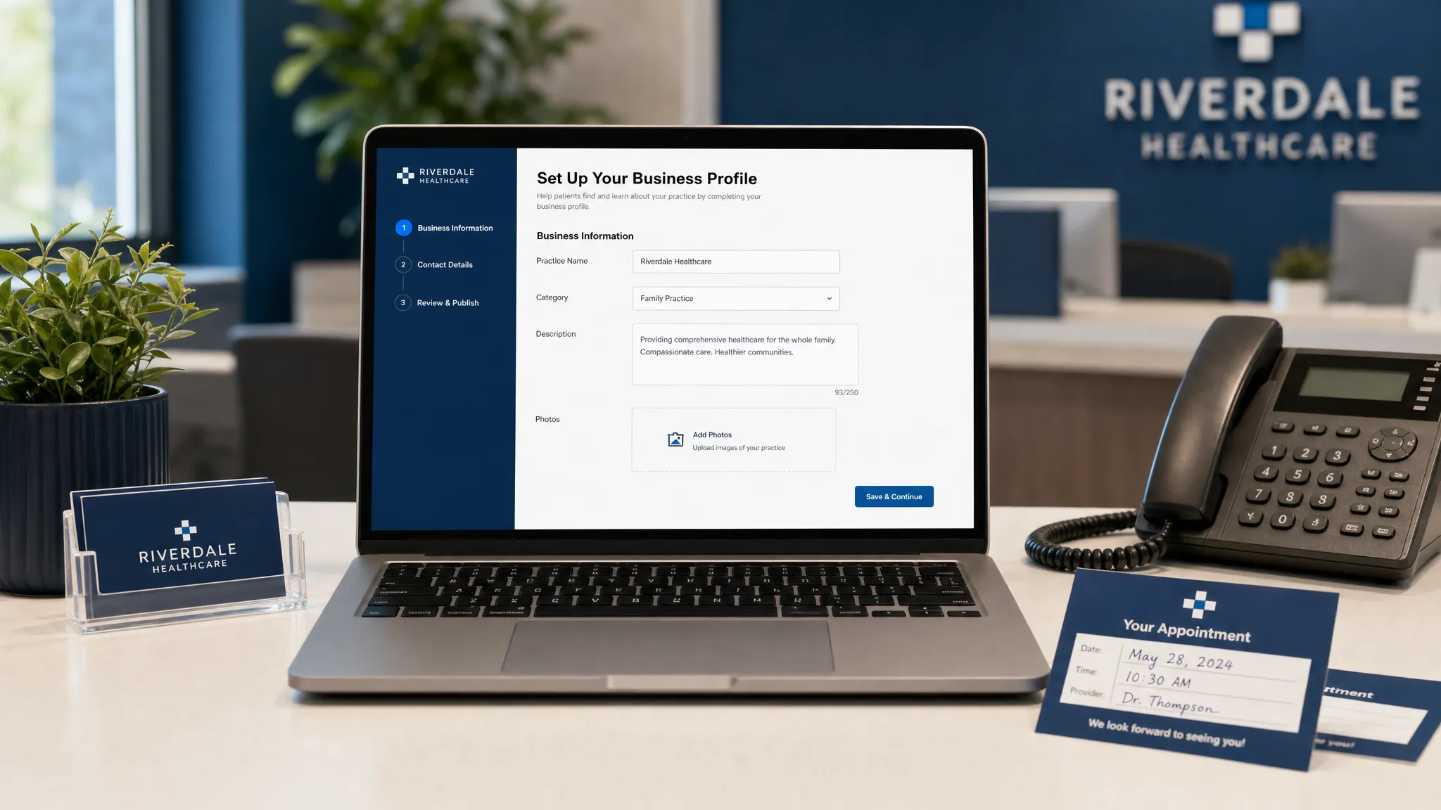 A healthcare practice front desk workspace with a laptop screen facing the viewer and showing a clean local business profile setup form, with a phone, appointment cards, and a small plant on the desk.