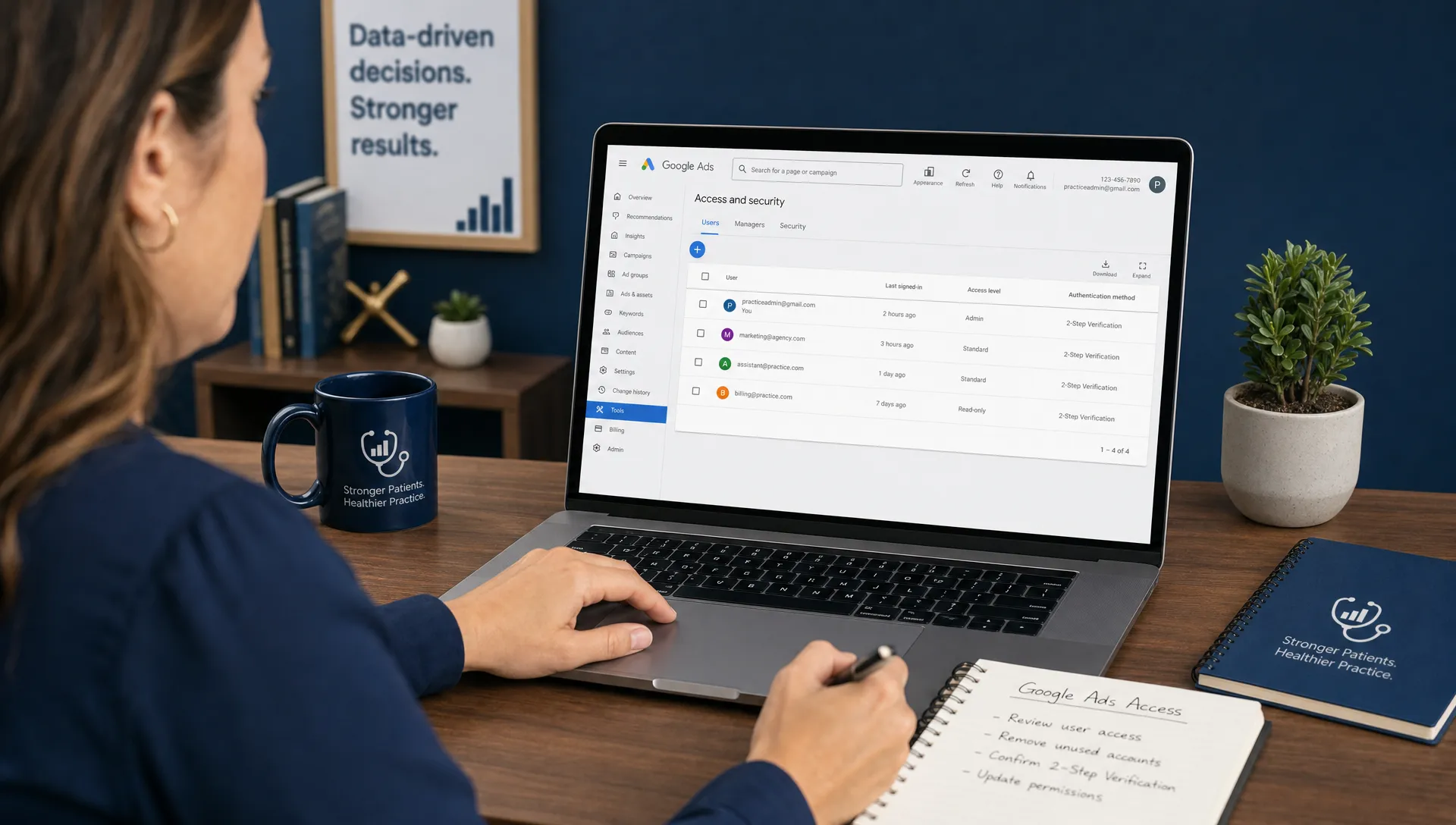 A practice administrator reviews Google Ads access settings at a desk with notes, a laptop screen facing the viewer, and a permissions dashboard.
