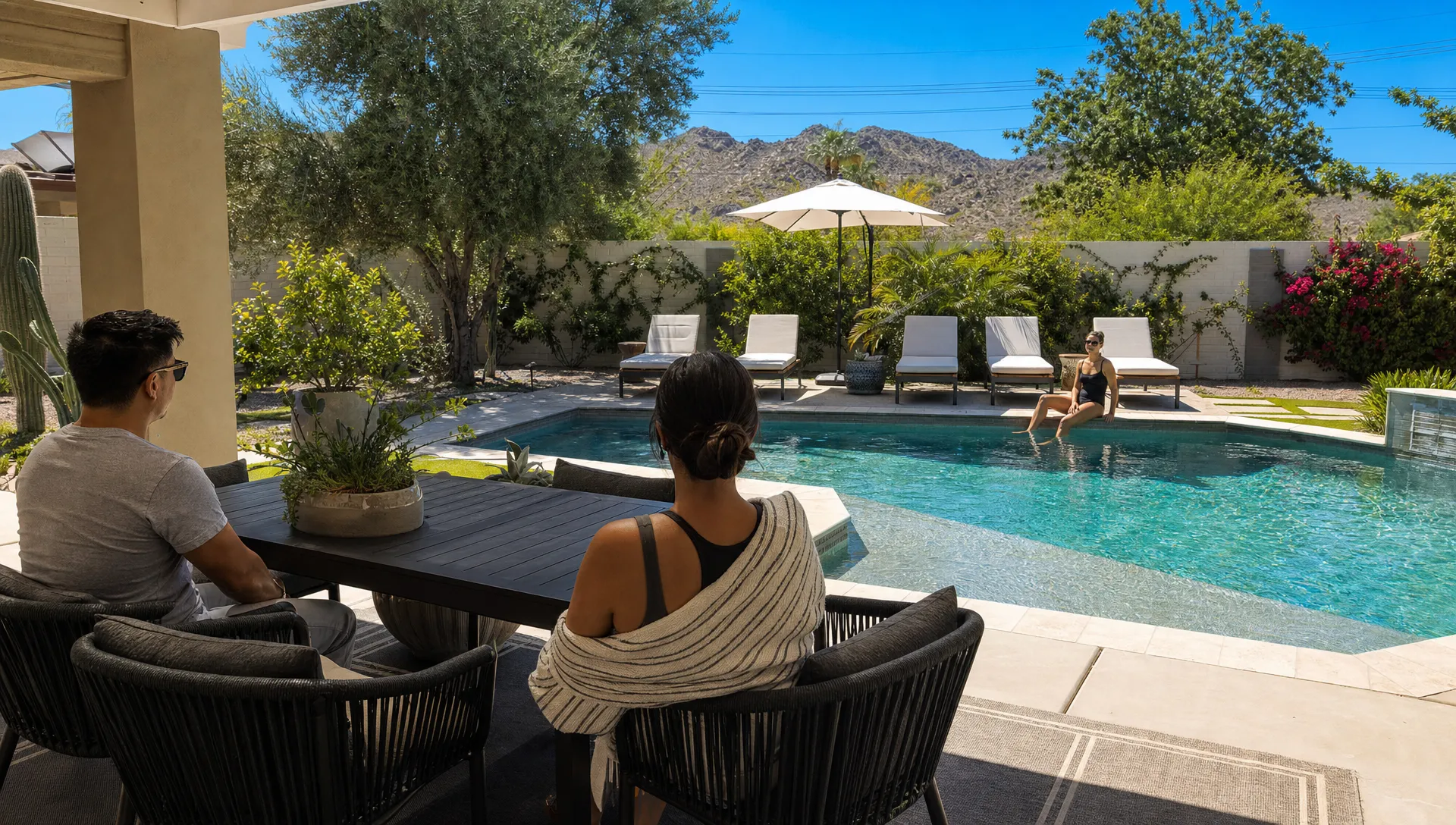 Guests relax by a shaded private pool at a Phoenix-area rental with desert landscaping and outdoor seating.
