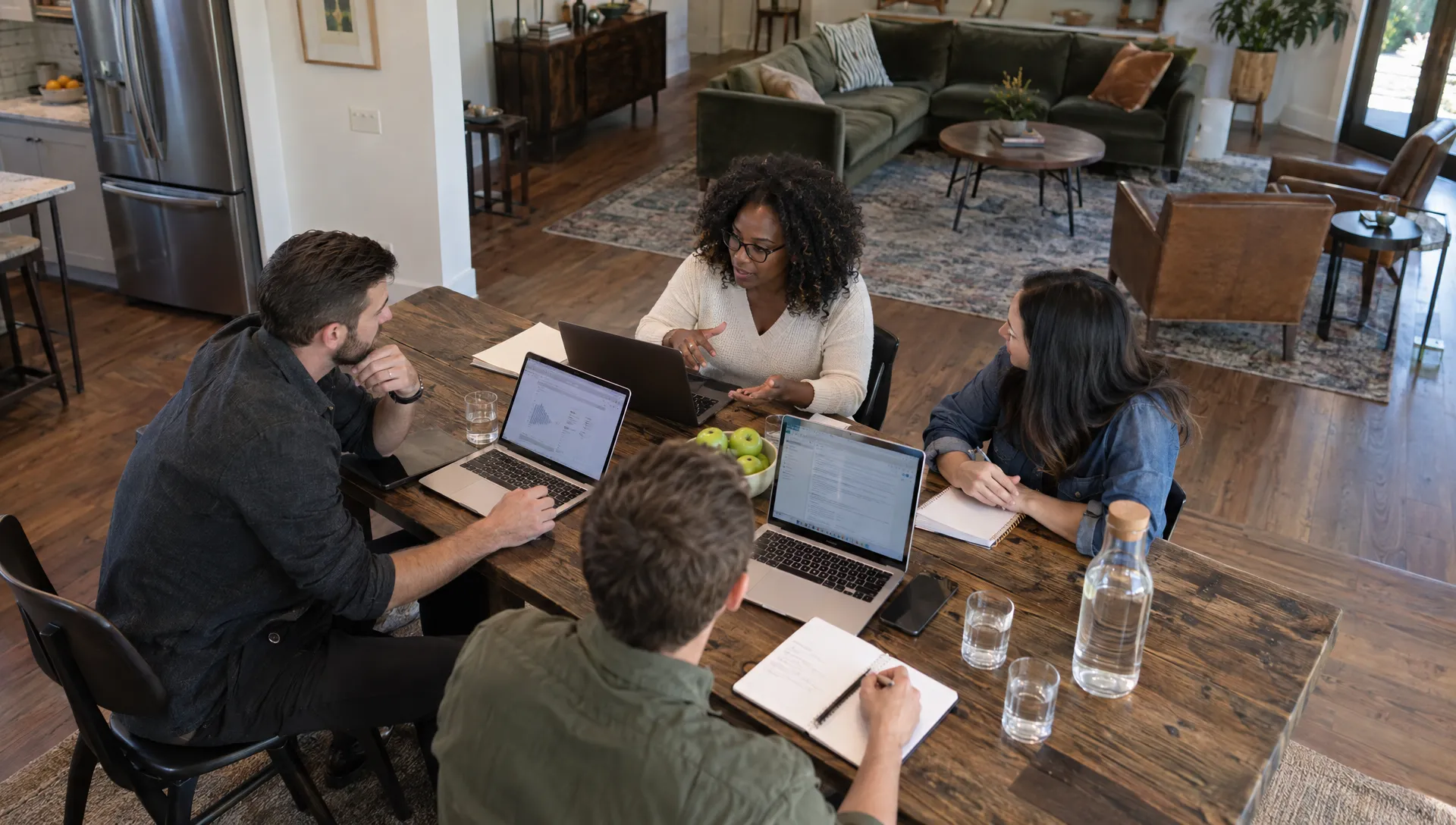 Four coworkers review a work plan at a private home's dining table beside a lounge for informal team conversations.