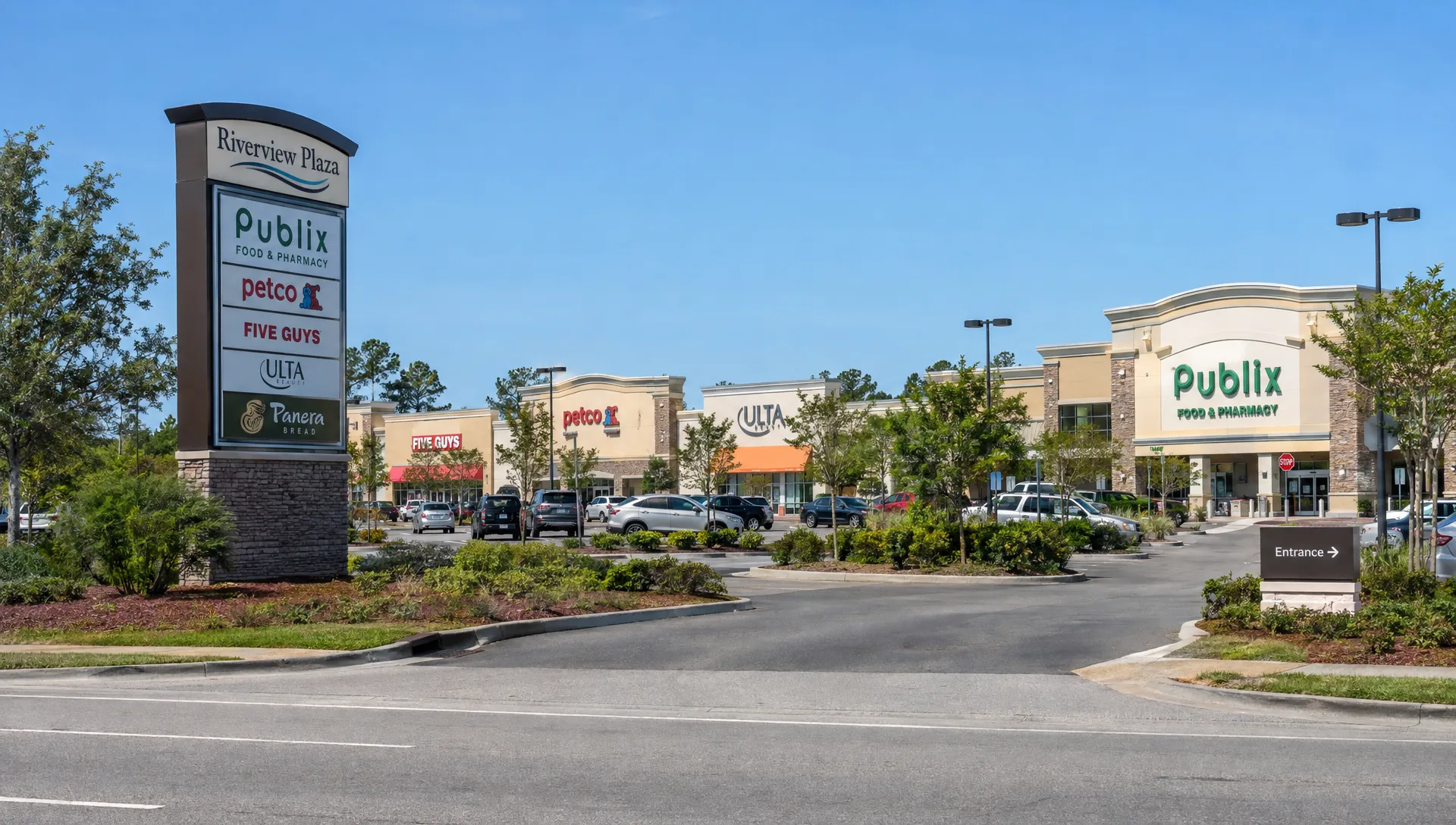 A pylon sign marks a retail plaza entrance, with storefronts set back along the driveway.